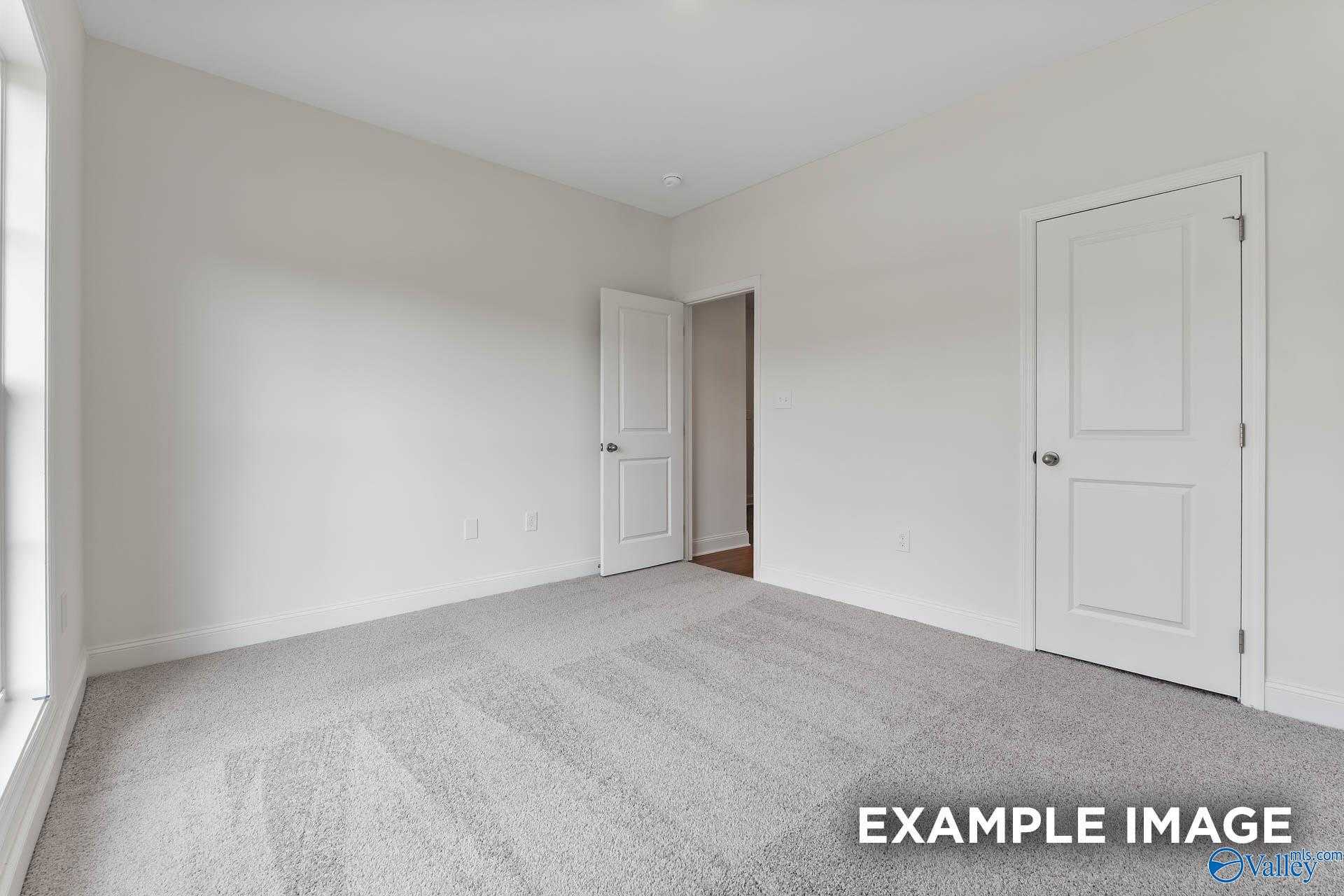 Empty bedroom with white walls, beige carpet, double doors, and large window in Davidson Homes The Daphne V, Athens, Alabama