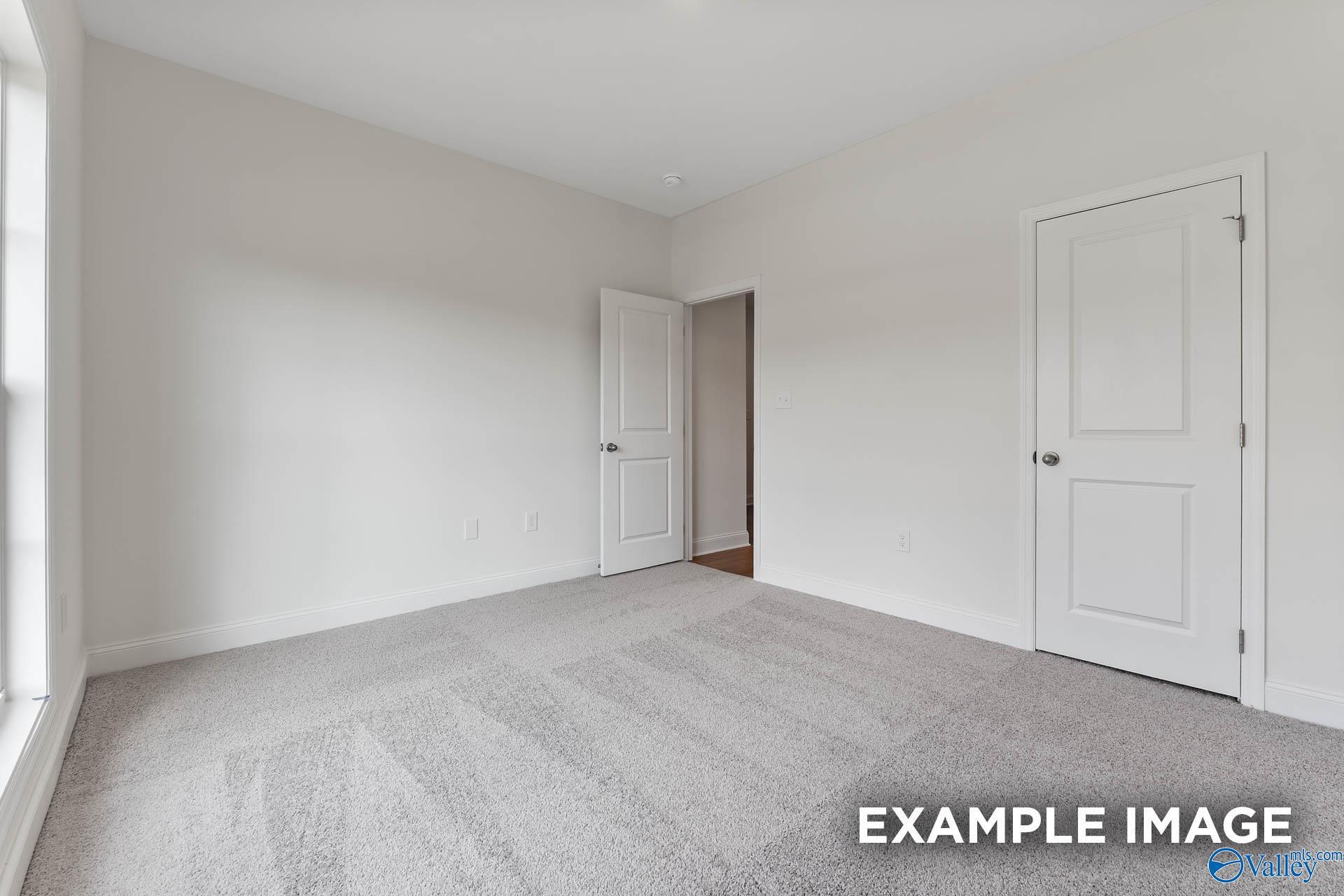 Empty bedroom with white walls, beige carpet, double doors, and large window in Davidson Homes The Daphne V, Athens, Alabama