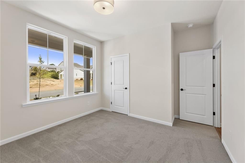 Bright bedroom with large windows overlooking wooded backyard, beige walls, gray carpet, white doors in Davidson Homes The Daphne B, Loganville GA