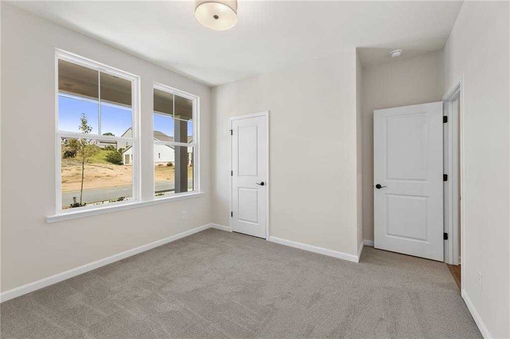 Bright bedroom with large windows overlooking wooded lot, white doors, beige walls, gray carpet in Davidson Homes The Daphne B, Loganville, GA