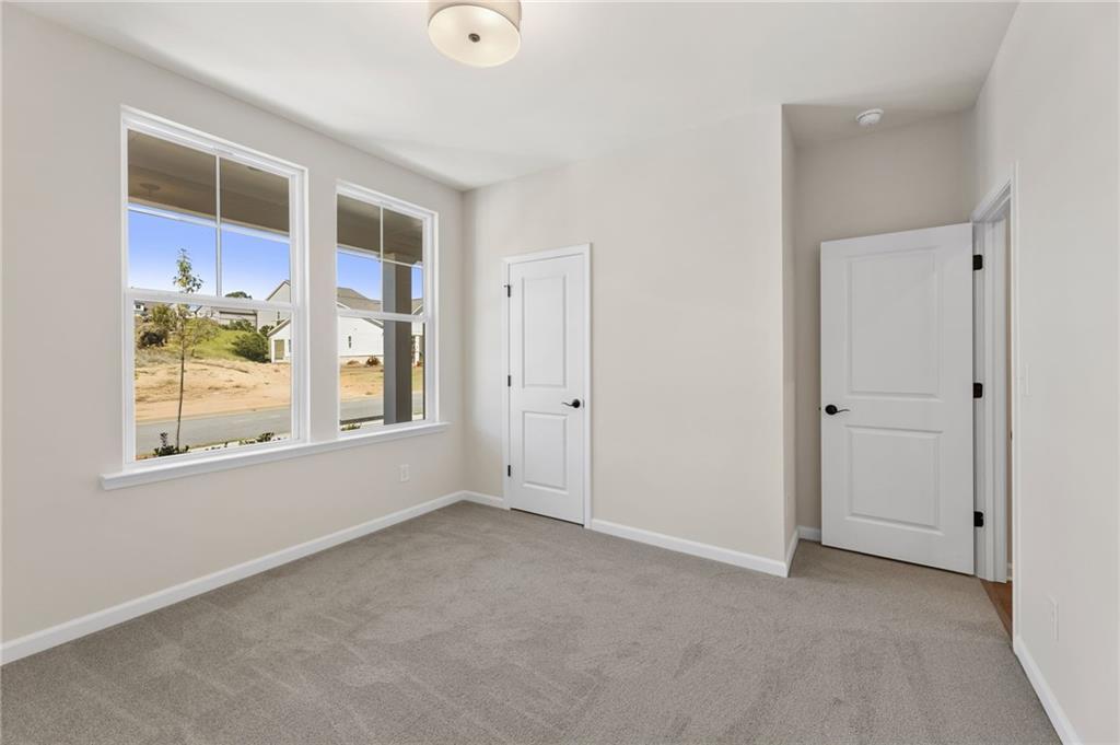 Bright bedroom with large windows overlooking wooded backyard, beige walls, gray carpet, white doors in Davidson Homes The Daphne B, Loganville GA