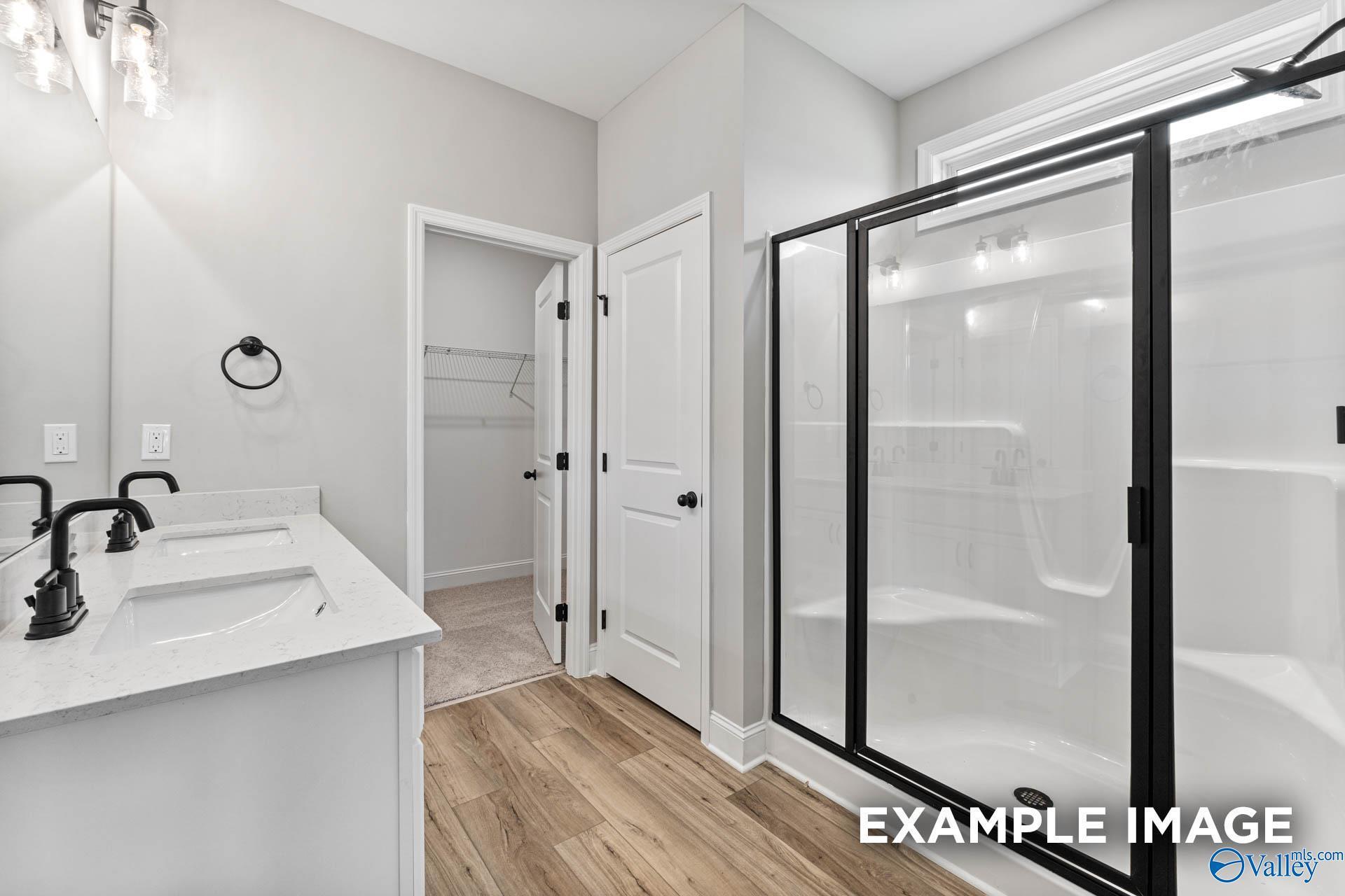 Modern master bathroom with double quartz vanity, black fixtures, glass shower, and walk-in closet in Davidson Homes Franklin C, Athens AL
