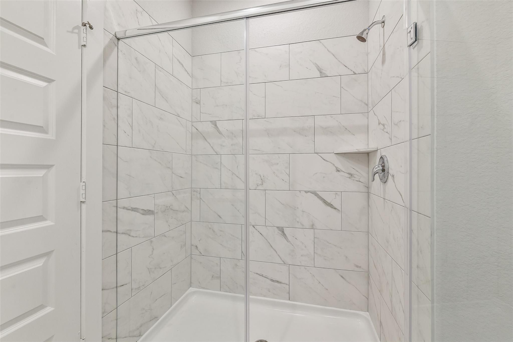 Elegant walk-in shower with white subway tiles, frameless glass door, and built-in bench in Davidson Homes The Colorado G, Magnolia TX