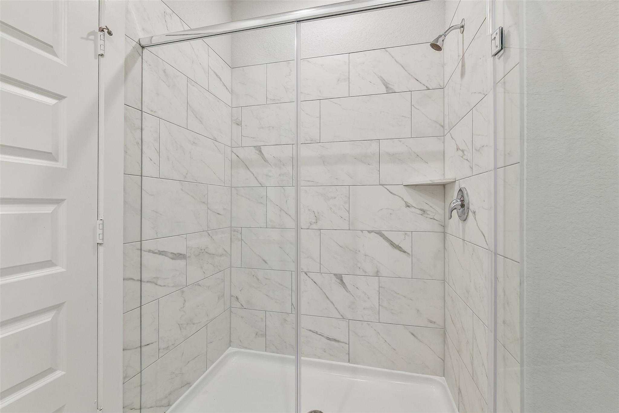 Elegant walk-in shower with white subway tiles, frameless glass door, and built-in bench in Davidson Homes The Colorado G, Magnolia TX