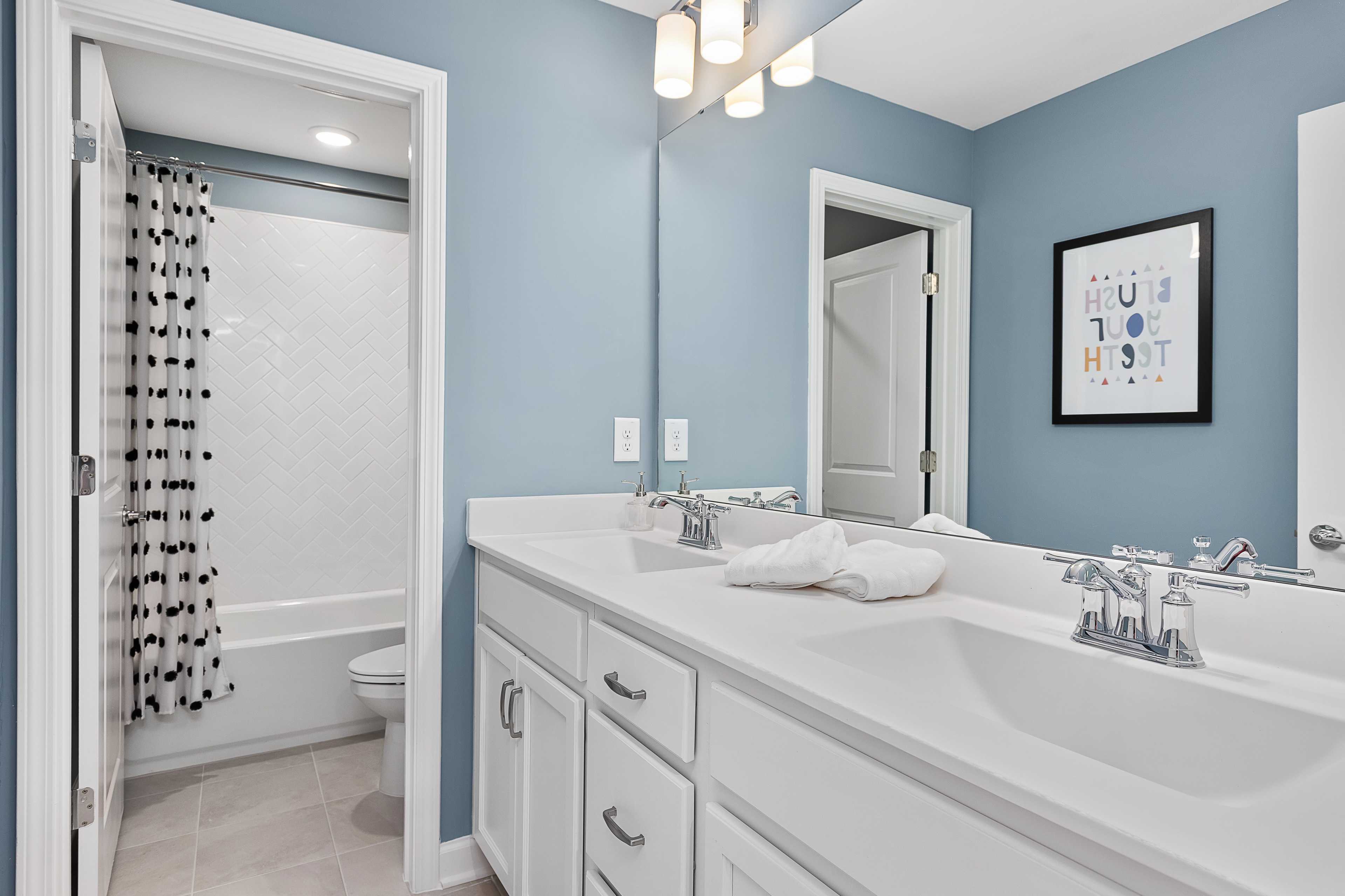 Light blue kids' bathroom at Woodland Crossing in Zebulon NC with double vanity, bathtub, and subway tile