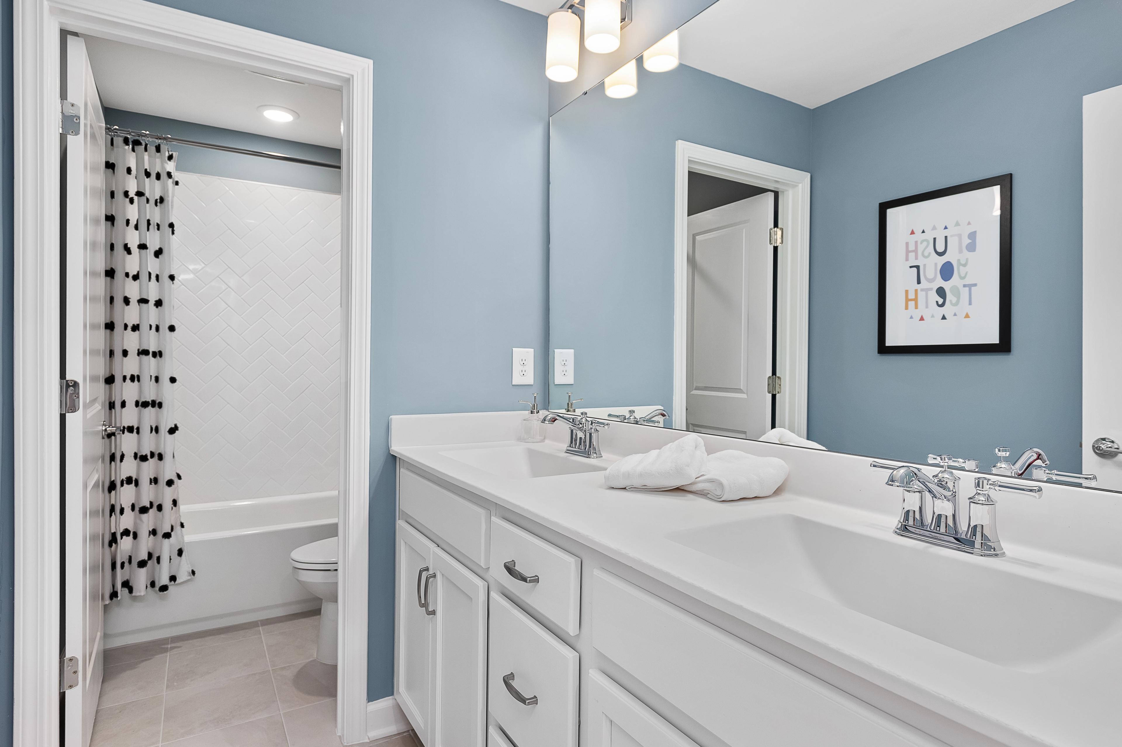 Light blue kids' bathroom at Woodland Crossing in Zebulon NC with double vanity, bathtub, and subway tile