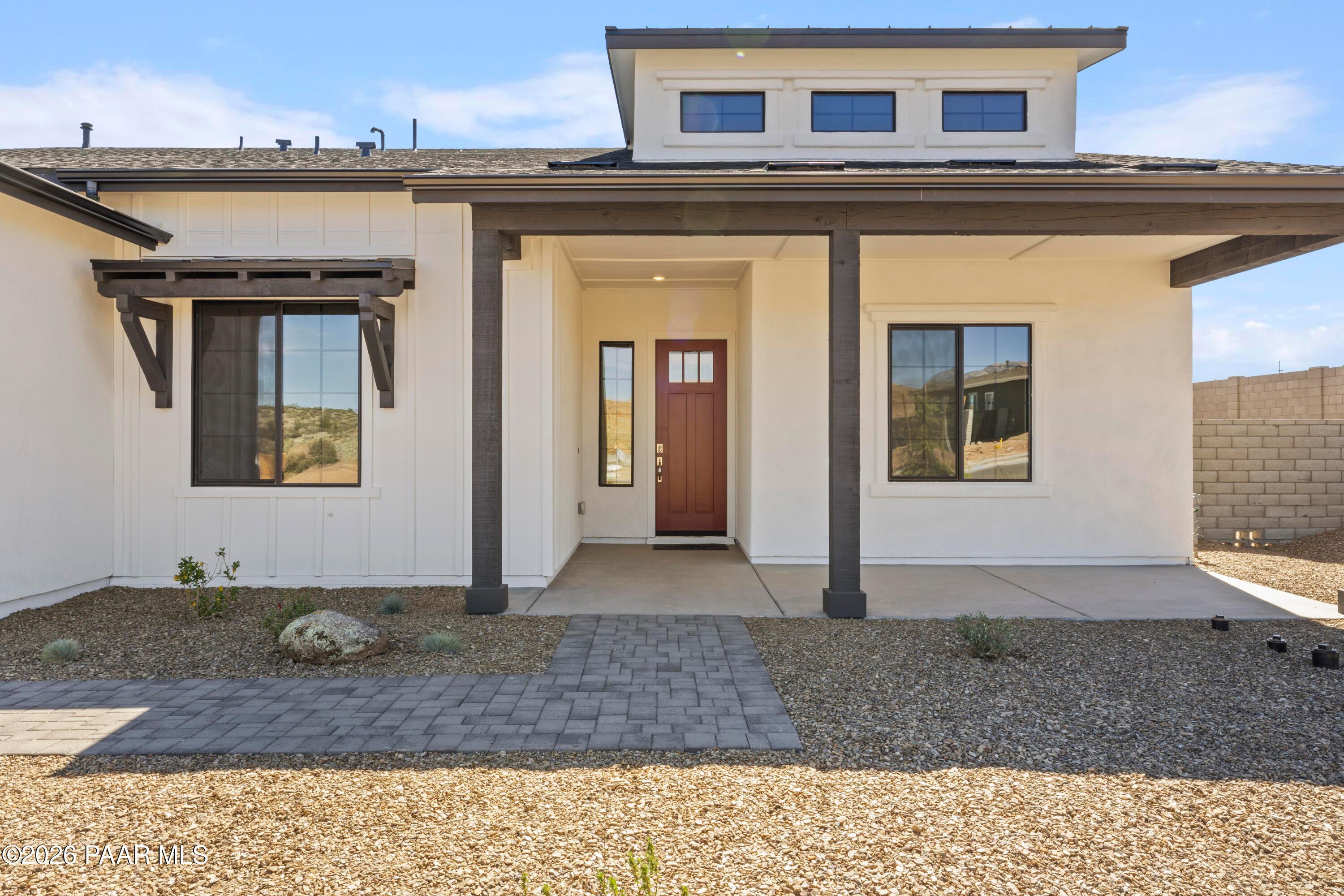 Modern single-story home facade with beige stucco, dark trim, red door, and covered entry in Hidden Hills, Prescott, Arizona