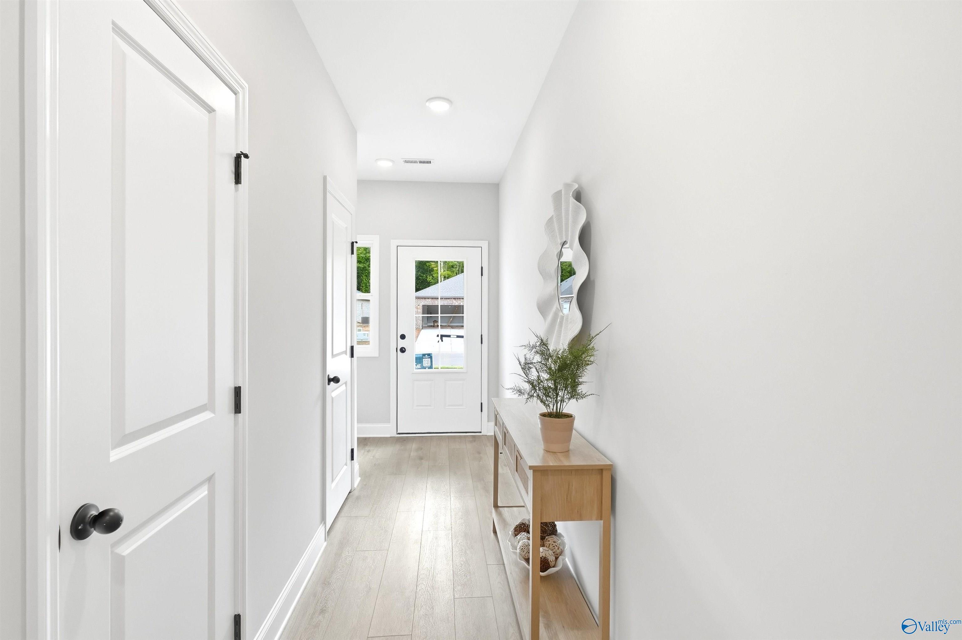Bright white entry foyer with luxury vinyl plank floors, glass-panel front door, and wood console table in Davidson Homes' The Russell A, Huntsville