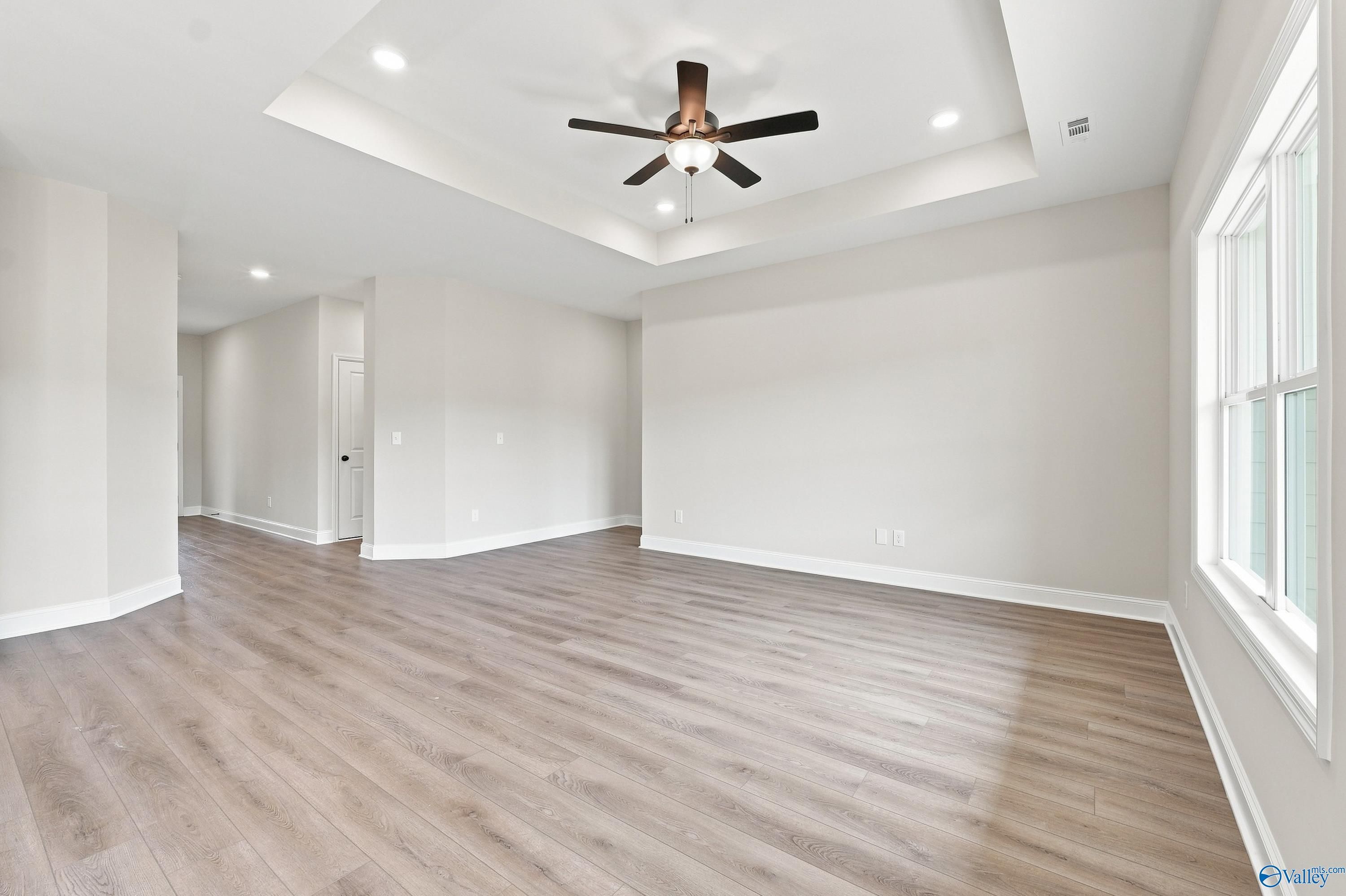 Spacious living room with tray ceiling and wood-style flooring in The Asheville E floor plan, Forest Glen, Hazel Green, AL.