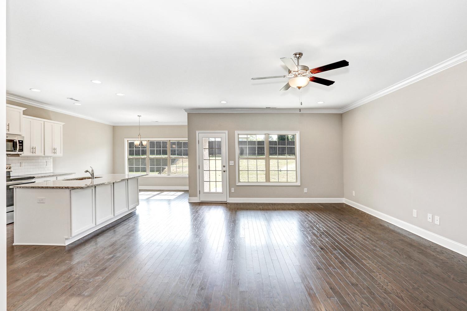 Open-concept kitchen and living area in The Montgomery by Davidson Homes, with white cabinetry, large island, hardwood floors, and large windows