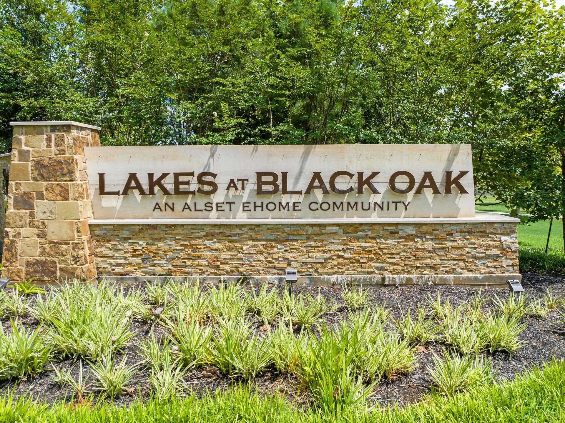 Entrance sign for Lakes at Black Oak all-age home community in Magnolia, Texas, with stone pillars and lush greenery