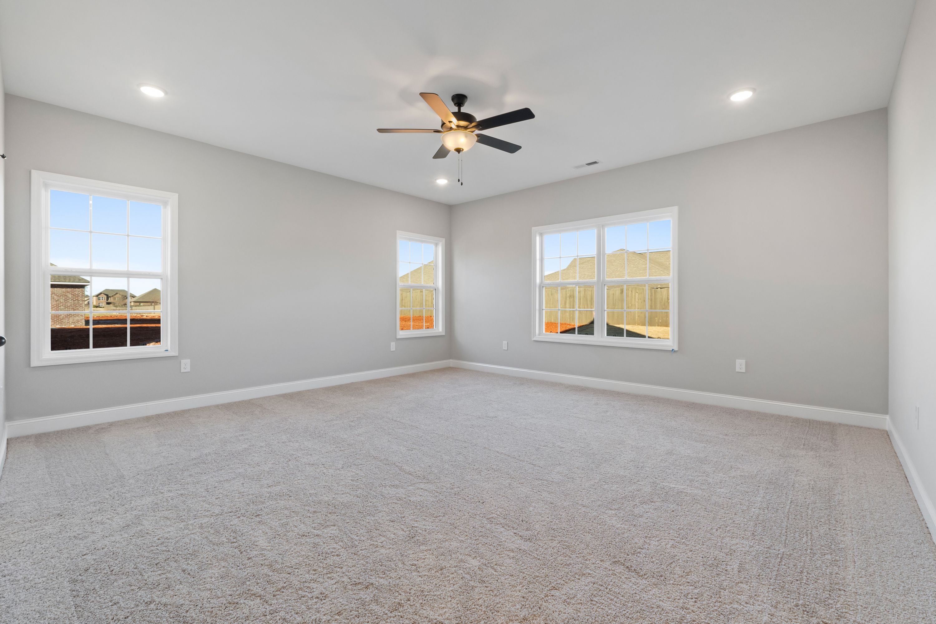 Spacious bedroom in The Valencia home by Davidson Homes featuring light gray walls, large windows, ceiling fan, and carpeted floor