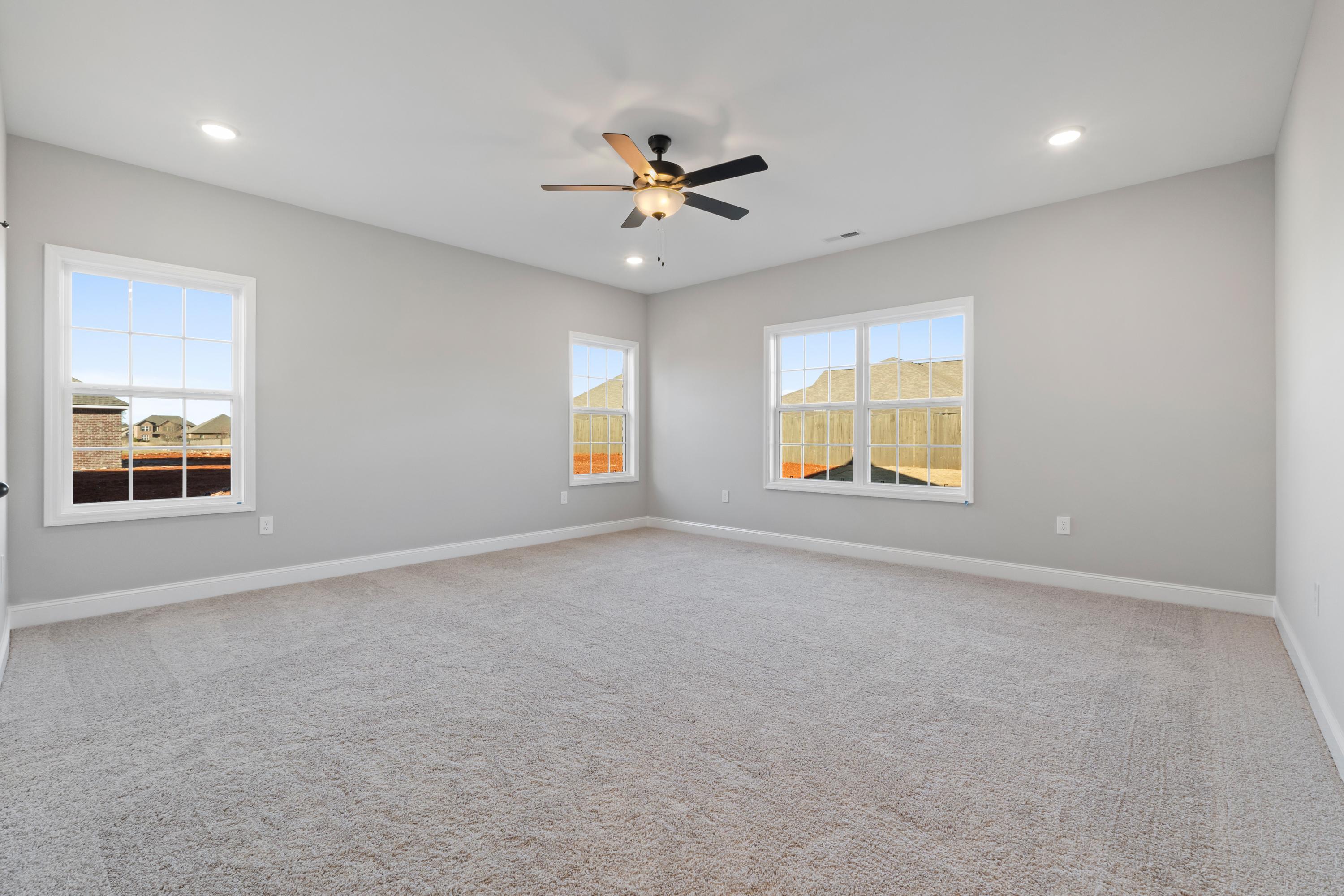Spacious bedroom in The Valencia home by Davidson Homes featuring light gray walls, large windows, ceiling fan, and carpeted floor