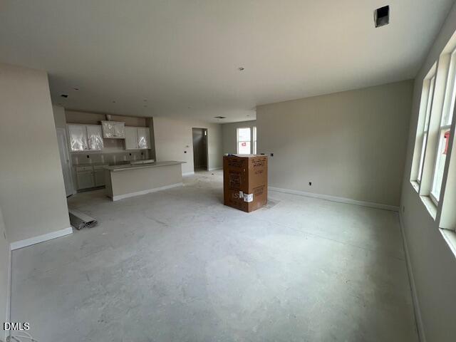 Open-concept kitchen and living area with white cabinets, bare floors, and large windows in unfinished 4-bedroom Davidson Homes The Preston A, Lillington, NC