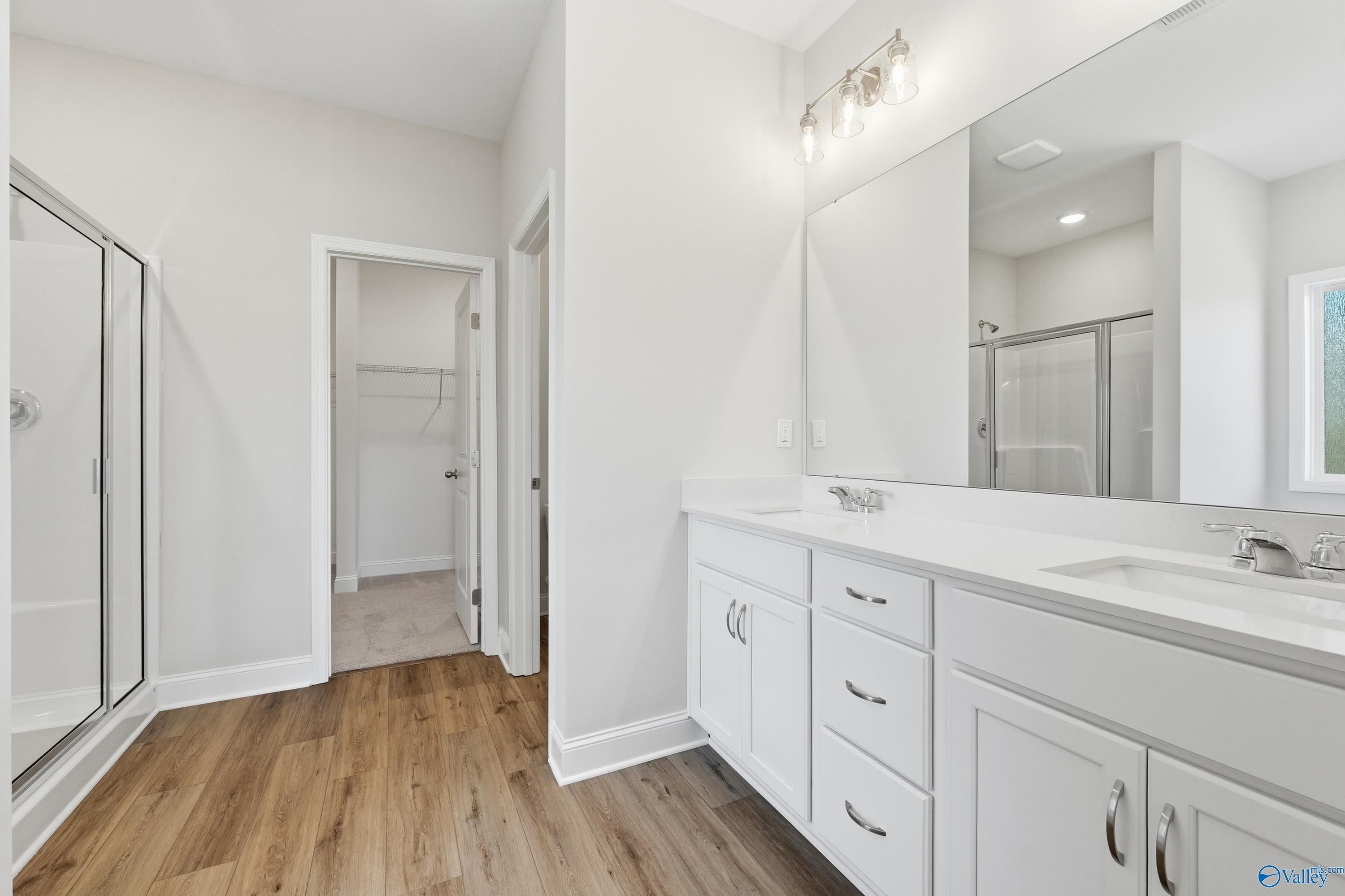 Modern master bathroom featuring double white vanity, large mirror, frameless glass shower, and walk-in closet in Davidson Homes The Everett, Harvest AL