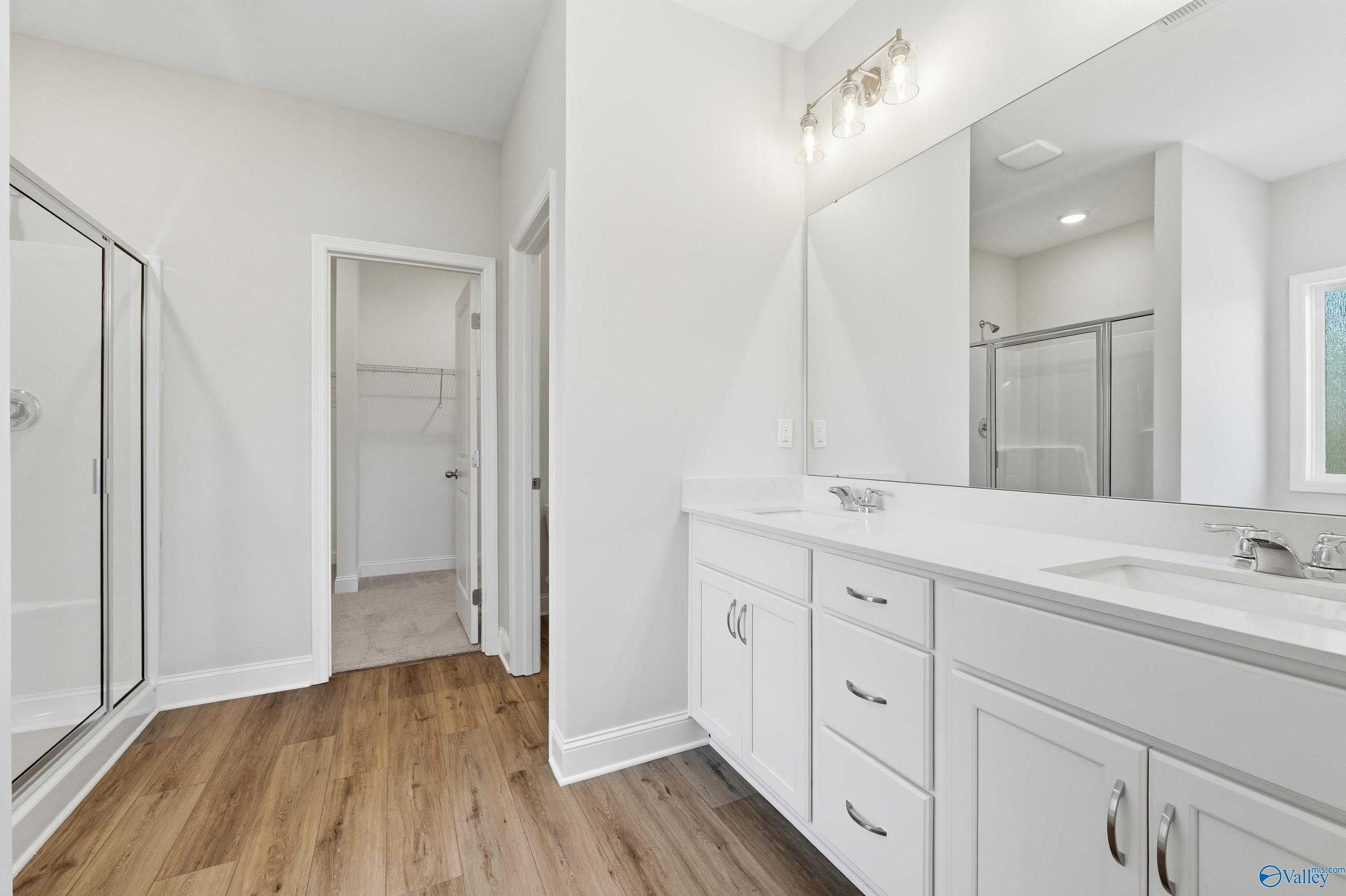 Modern master bathroom featuring double white vanity, large mirror, frameless glass shower, and walk-in closet in Davidson Homes The Everett, Harvest AL