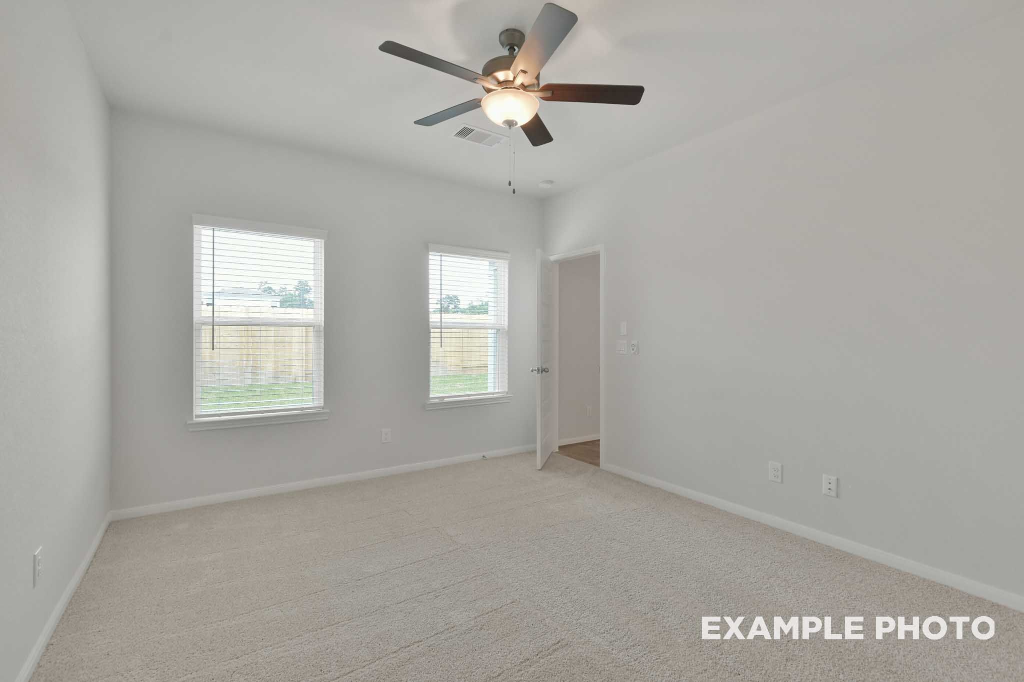 Bright spacious bedroom in The Brazos by Davidson Homes with ceiling fan, dual windows, and plush carpeting.