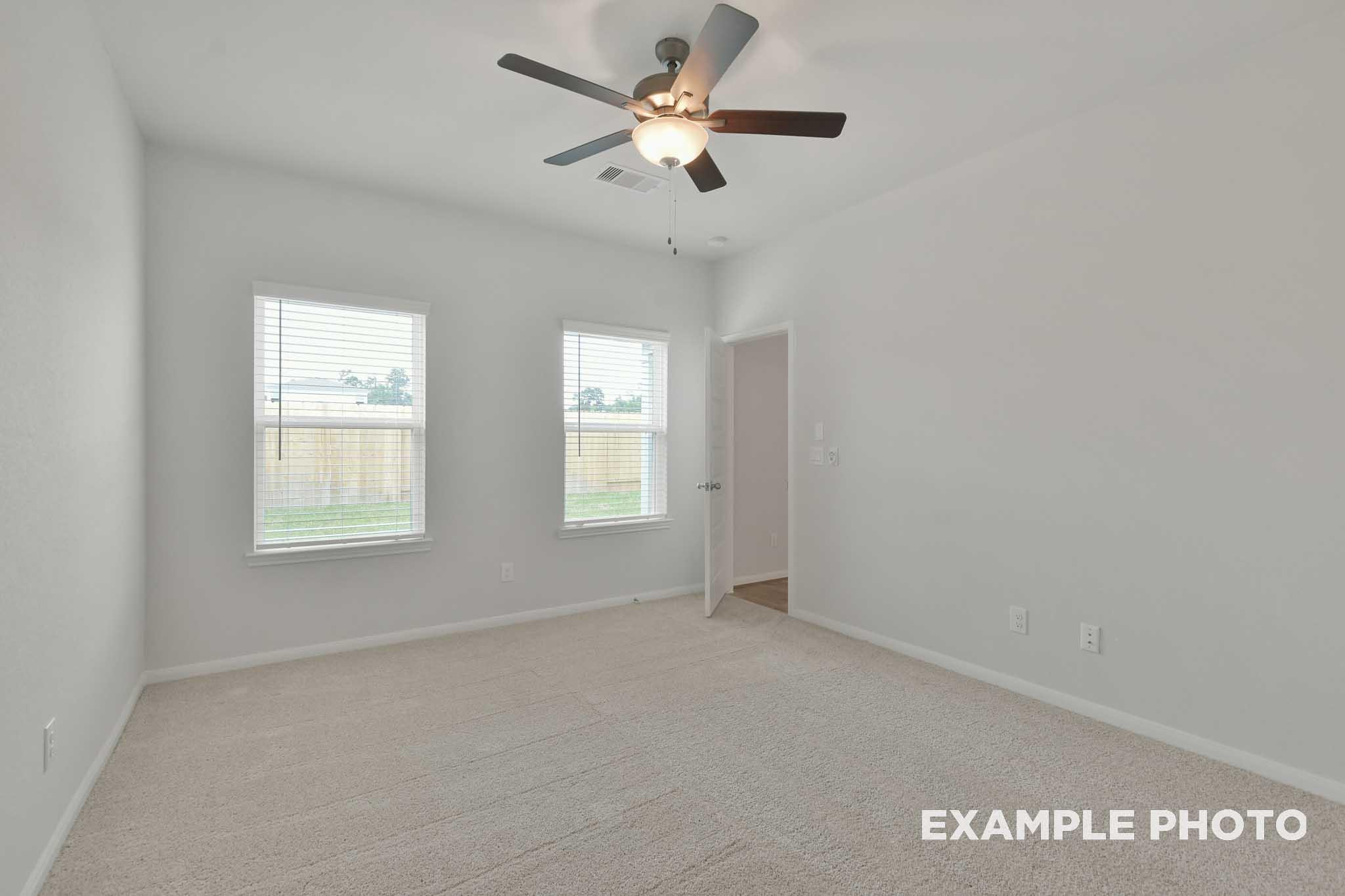 Bright spacious bedroom in The Brazos by Davidson Homes with ceiling fan, dual windows, and plush carpeting.