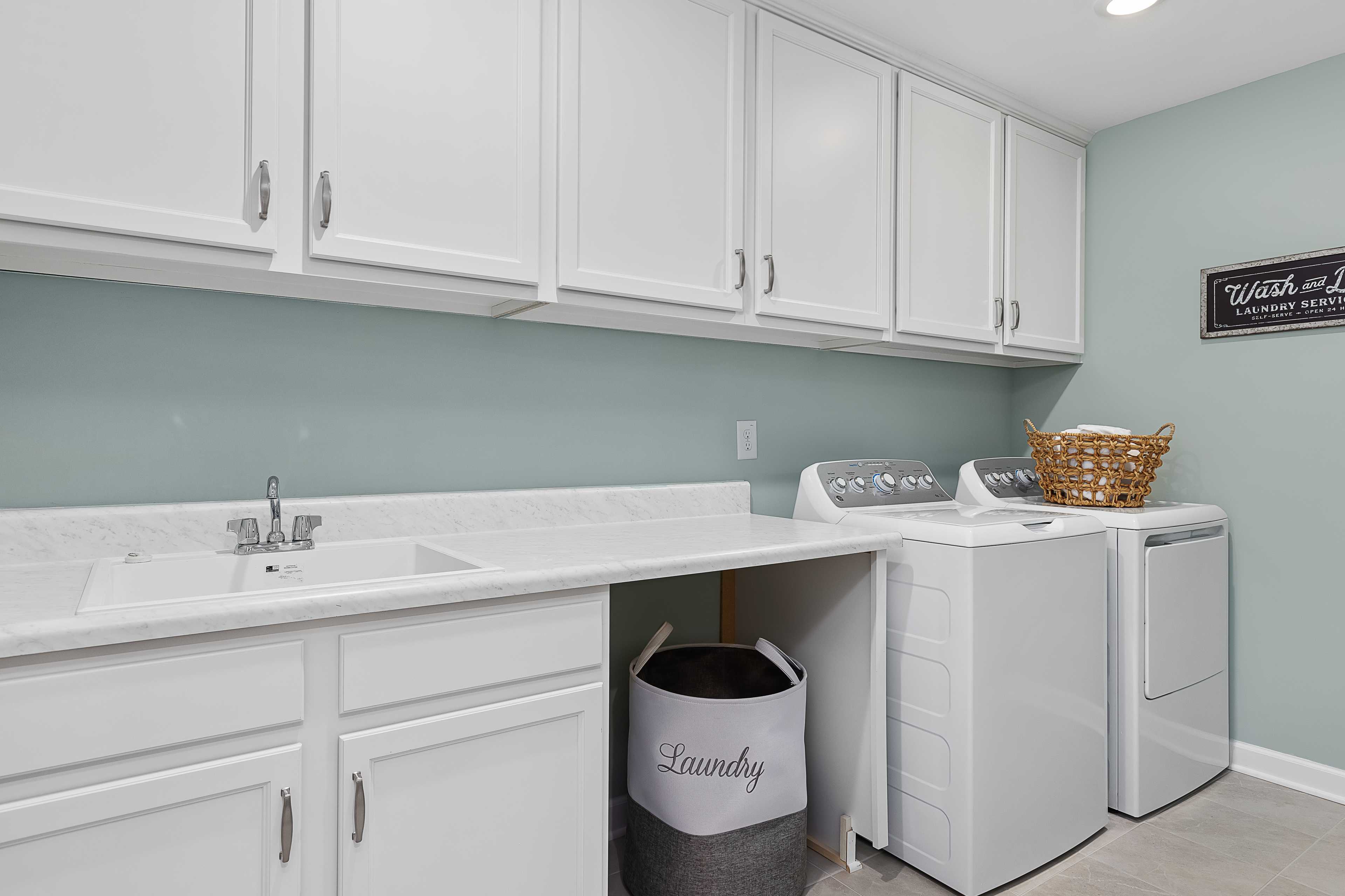 Spacious laundry room in Woodland Crossing, Zebulon NC with white cabinets, washer dryer, utility sink by Davidson Homes