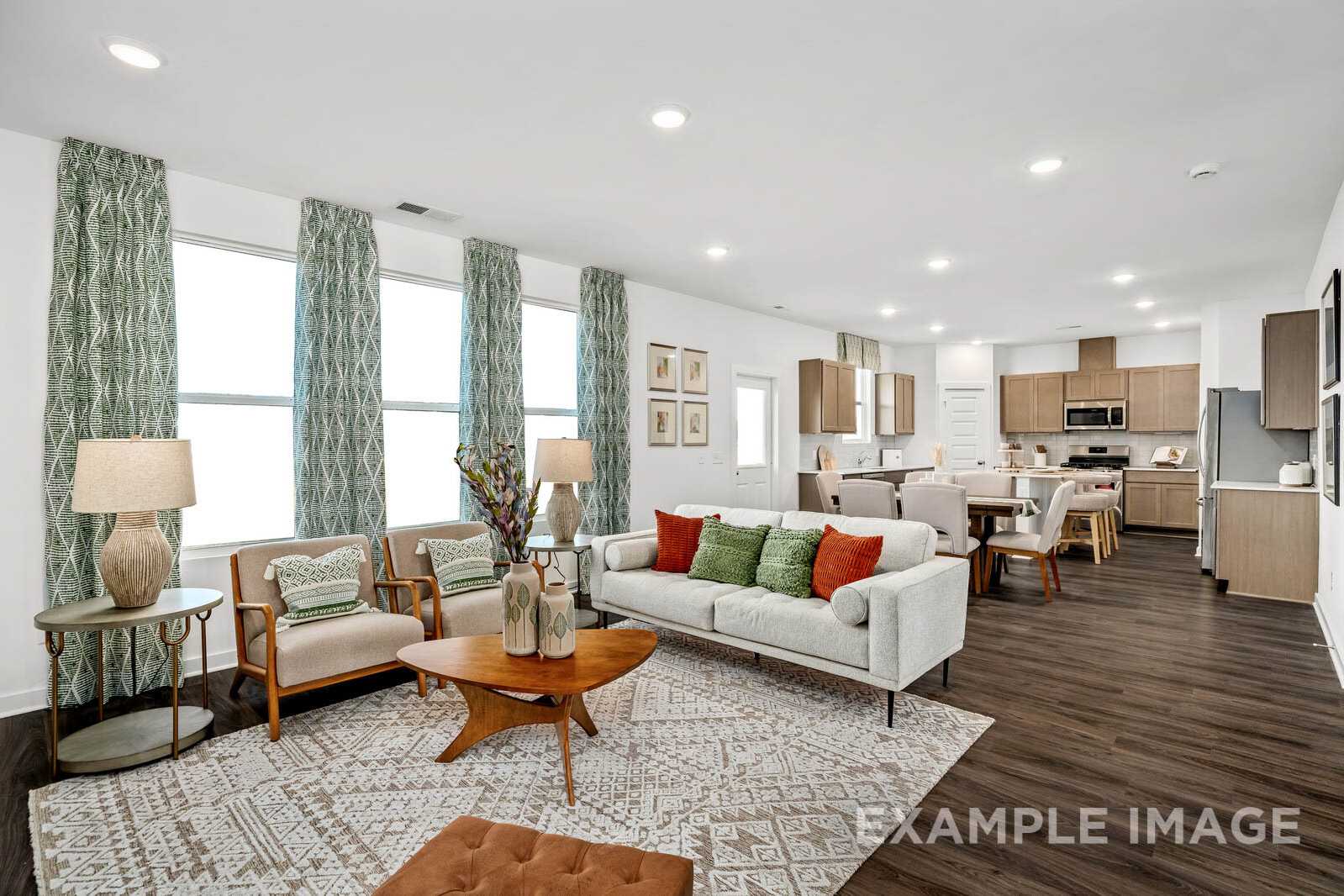 Spacious open-concept living room in The Gordon B with green sofa, wooden coffee table, teal curtains, and adjacent white kitchen by Davidson Homes