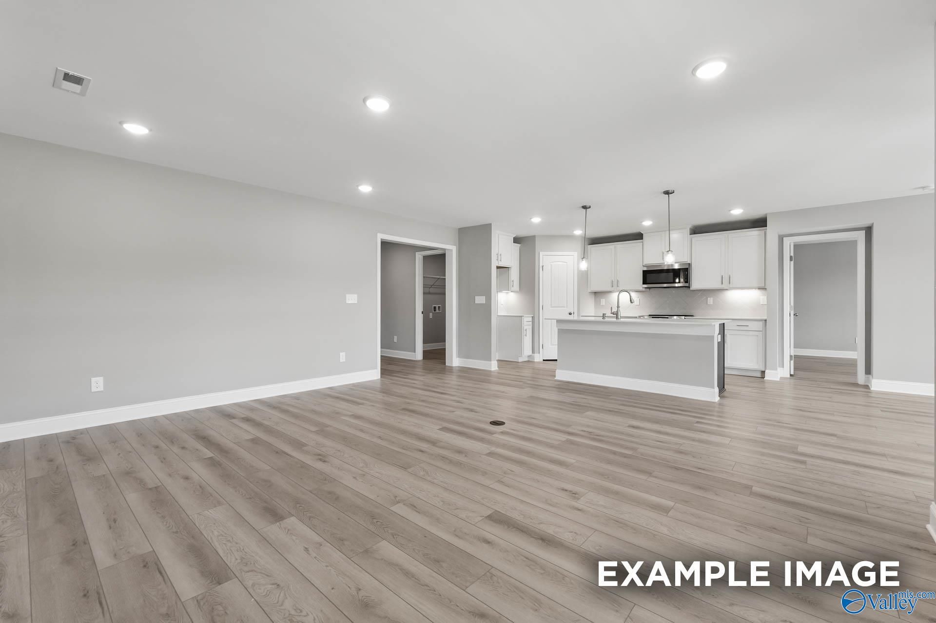 Spacious open-concept kitchen and living area with white cabinets, stainless microwave, light laminate floors in Everett B home, Toney, Alabama