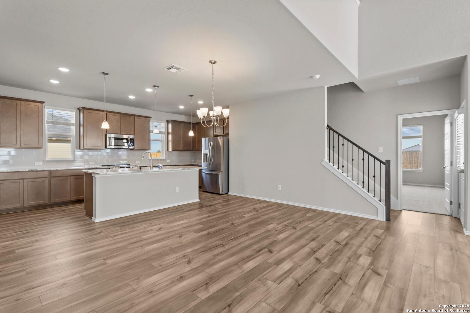 Modern open-concept kitchen with light wood cabinets, white quartz island, stainless appliances, and hardwood floors in The Collin B, Seguin, Texas