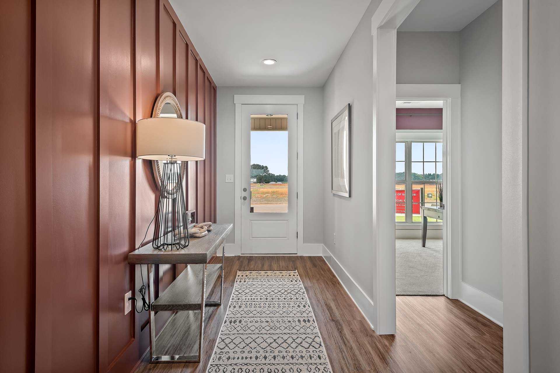 Spacious entry foyer at Heritage Lakes in New Market Alabama featuring red shiplap walls, console table with lamp, hardwood floors and open door to fields