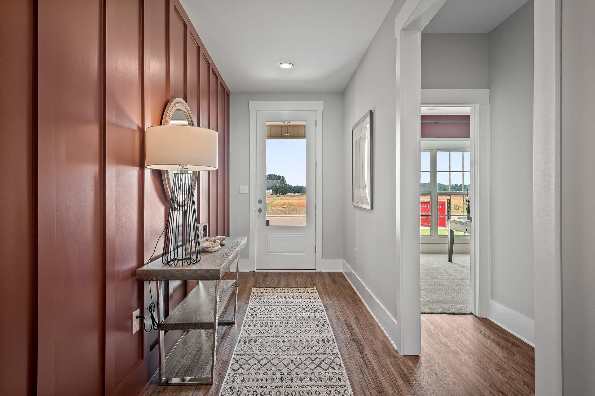 Spacious entry foyer at Heritage Lakes in New Market Alabama featuring red shiplap walls, console table with lamp, hardwood floors and open door to fields