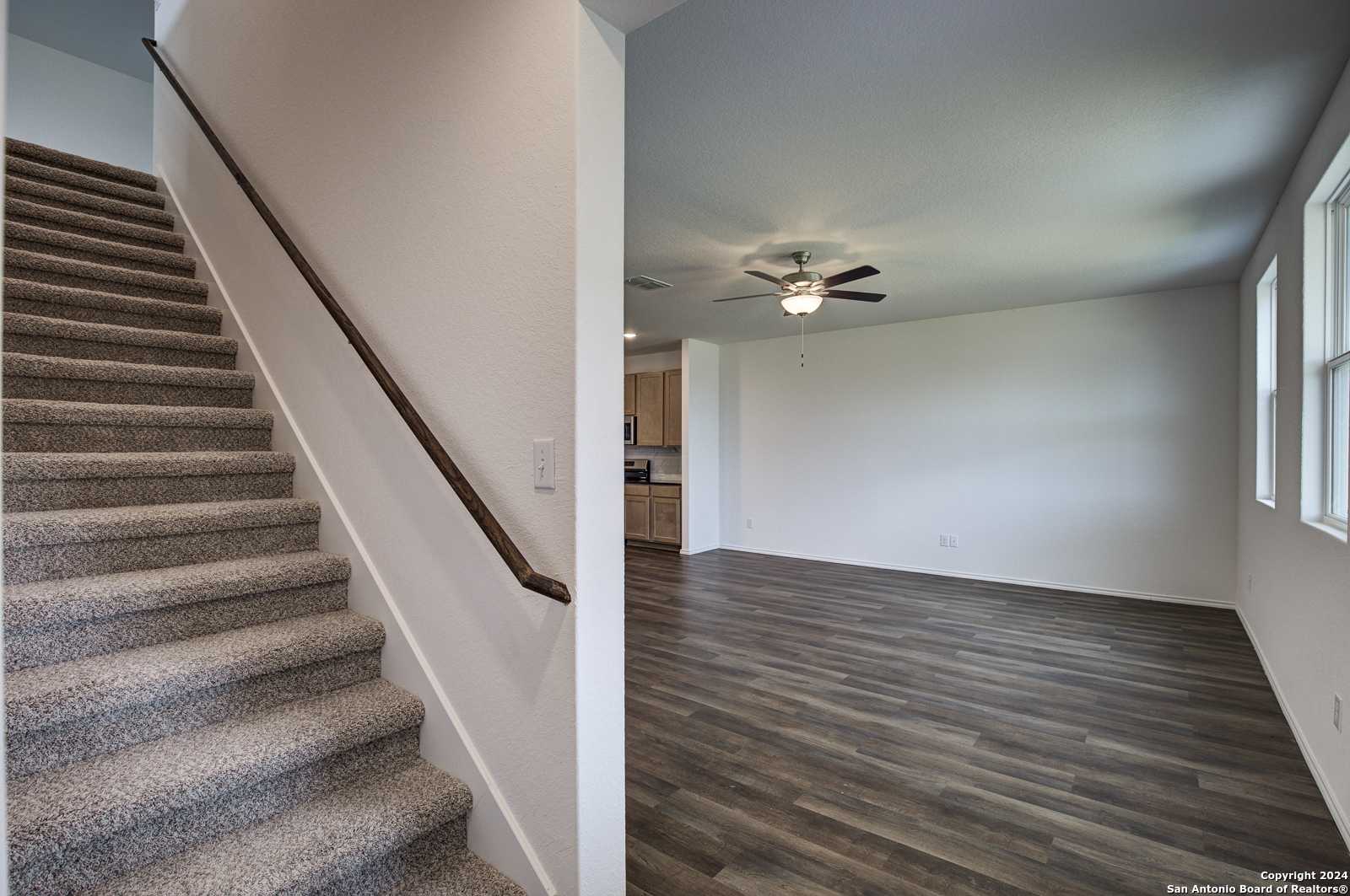Elegant carpeted staircase with wood handrail opening to hardwood-floor living area, ceiling fan, in Davidson Homes The Douglas D, Seguin, Texas