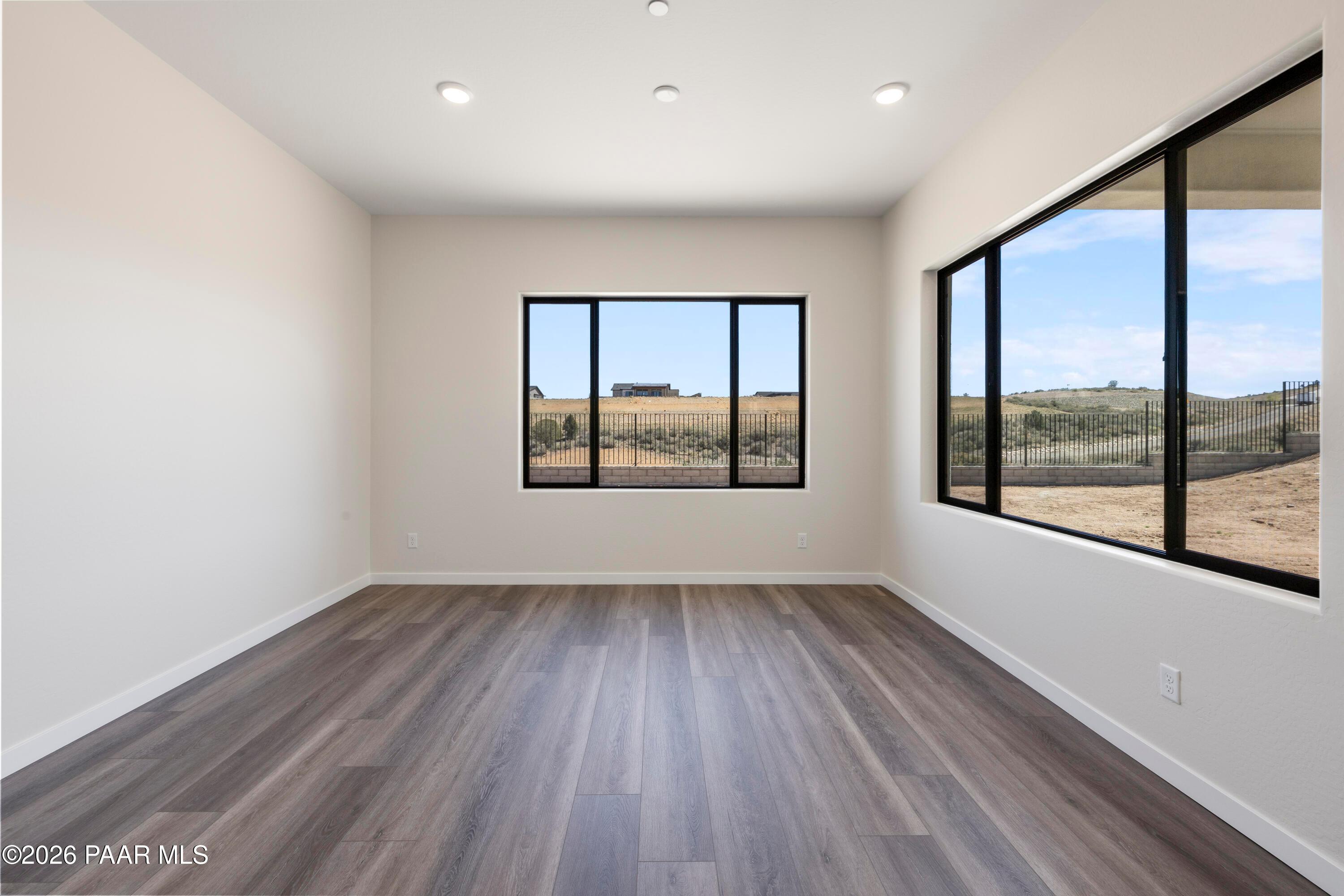 Bright empty living room with hardwood floors, beige walls, and large windows showcasing Prescott Arizona fields and hills in Soleil E home