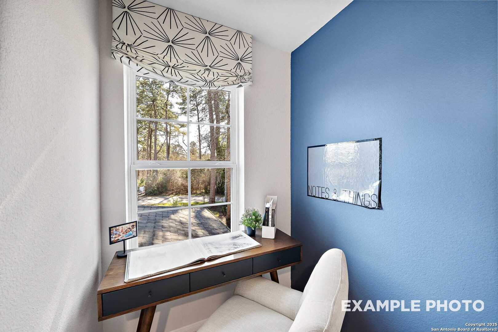Cozy home office with blue accent wall, window view of pine trees, wooden desk and armchair in Davidson Homes The San Marcos D, San Antonio