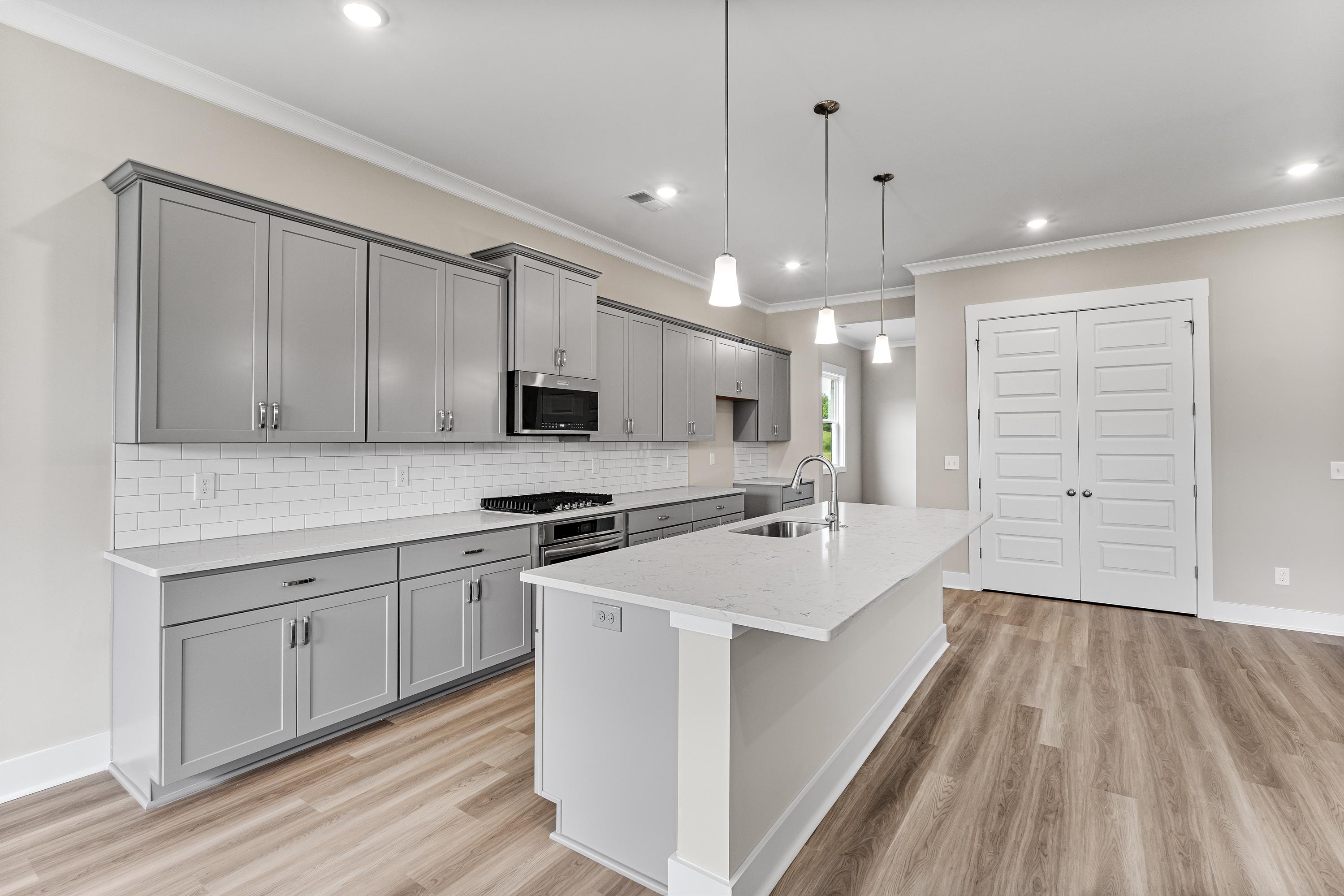 Modern kitchen in The Oxford A with gray shaker cabinets, white quartz island, subway tile backsplash, and open layout