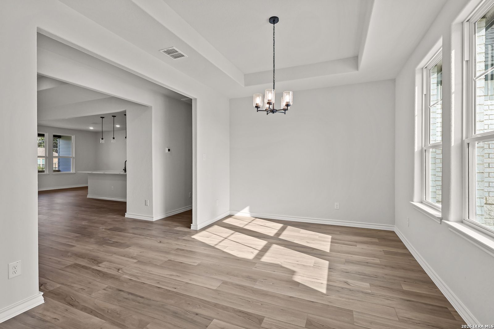 Bright dining room with wood-look flooring, chandelier, and tray ceiling in Davidson Homes Oxford F plan, Castroville, Texas