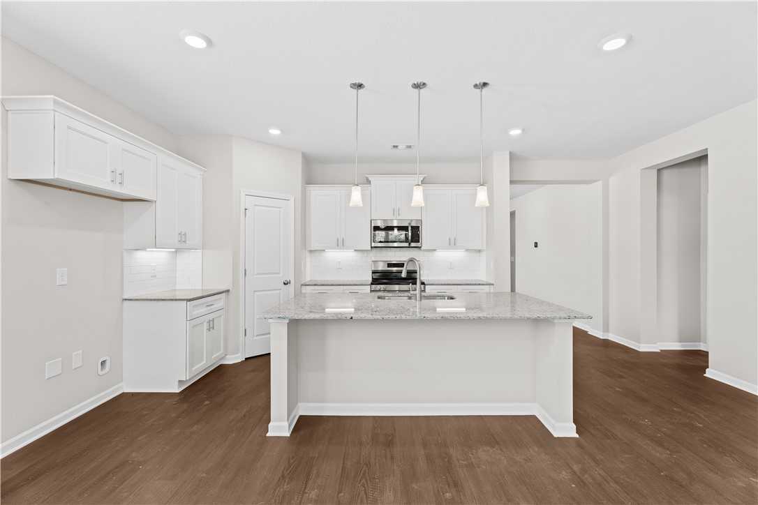 Modern white kitchen with granite island, stainless appliances, and pendant lights in Evermore Homes The Orion, Cusseta, AL