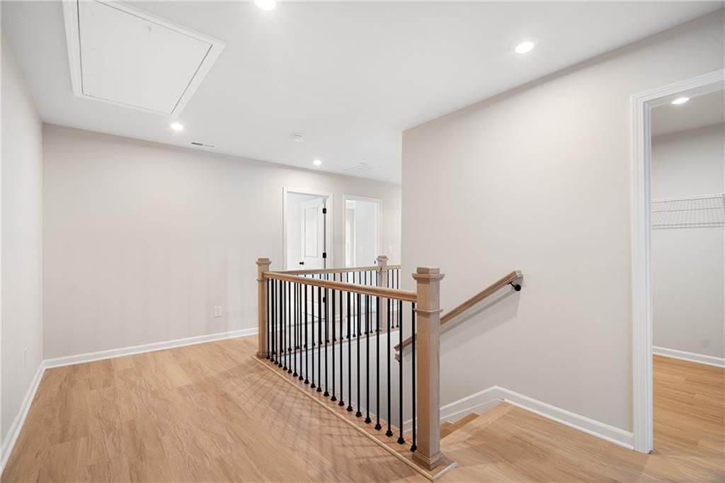 Upstairs hallway with hardwood floors, oak staircase railing, bedroom doors, and linen closet in Davidson Homes The Marion A, Kennesaw, GA