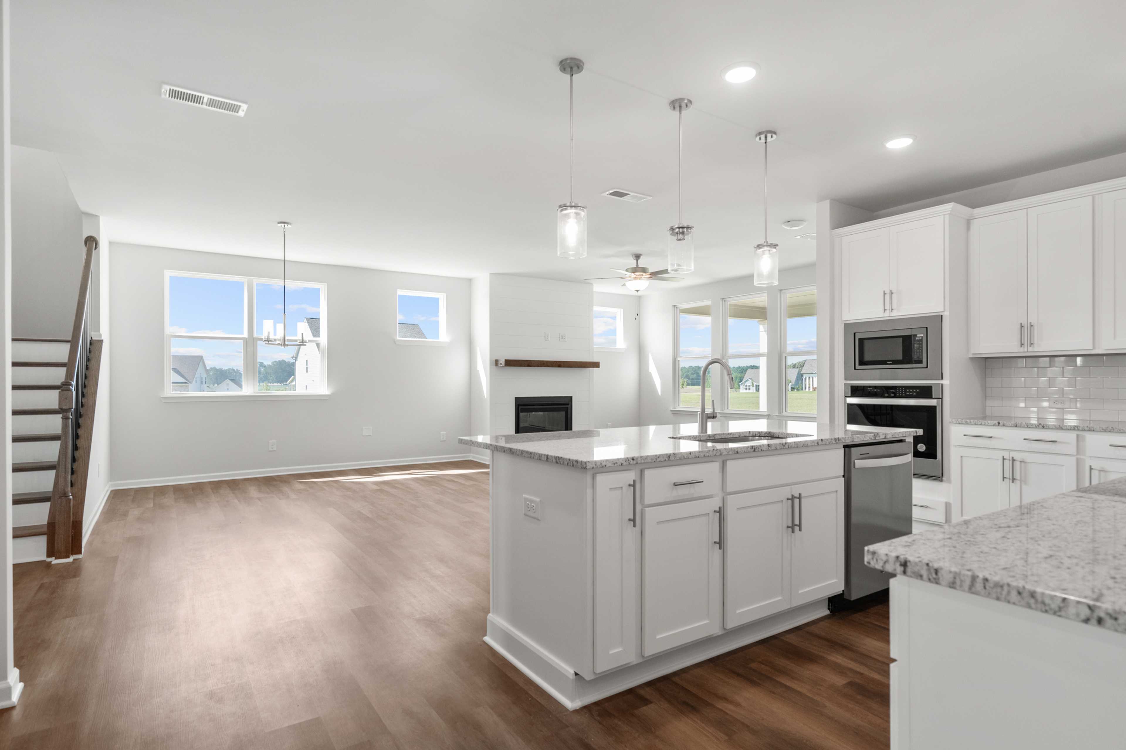 Open-concept kitchen and living room at Everleigh in Locust Grove GA by Davidson Homes with white cabinets granite island hardwood floors fireplace and large windows