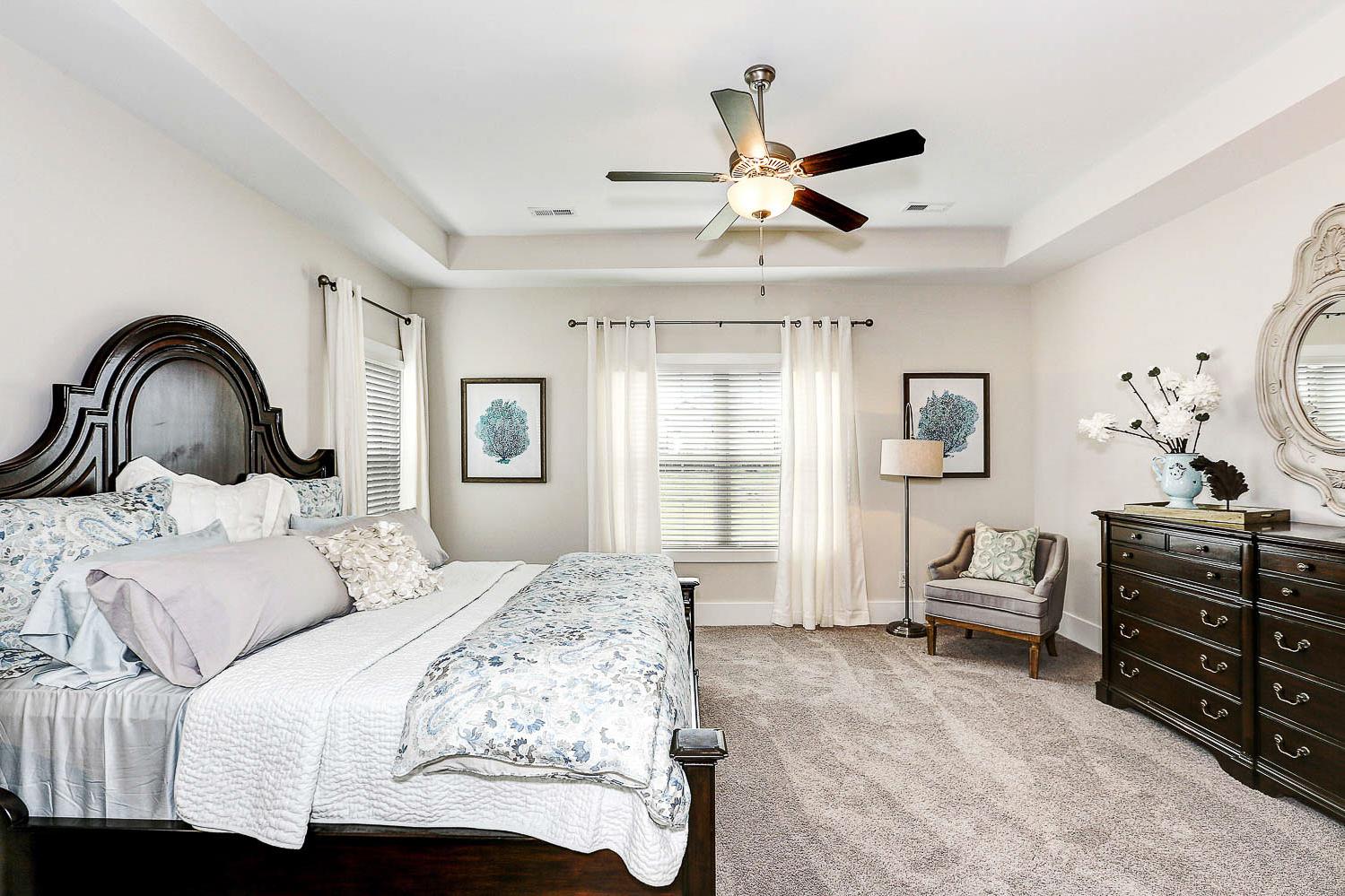 Elegant master bedroom in The Finleigh by Davidson Homes, featuring tufted king bed, dark wood dresser with mirror, armchair, and ceiling fan