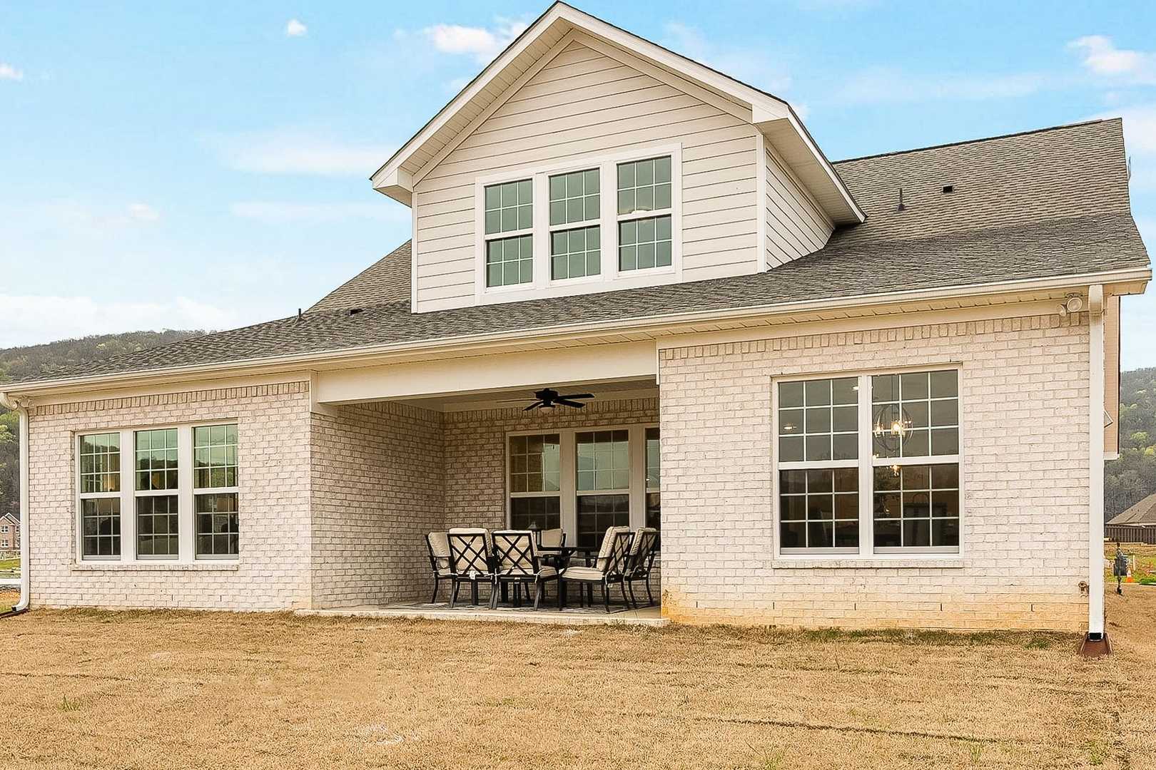 Rear elevation of The Oxford two-story home featuring covered patio, ceiling fan, outdoor seating, white brick siding, and large windows