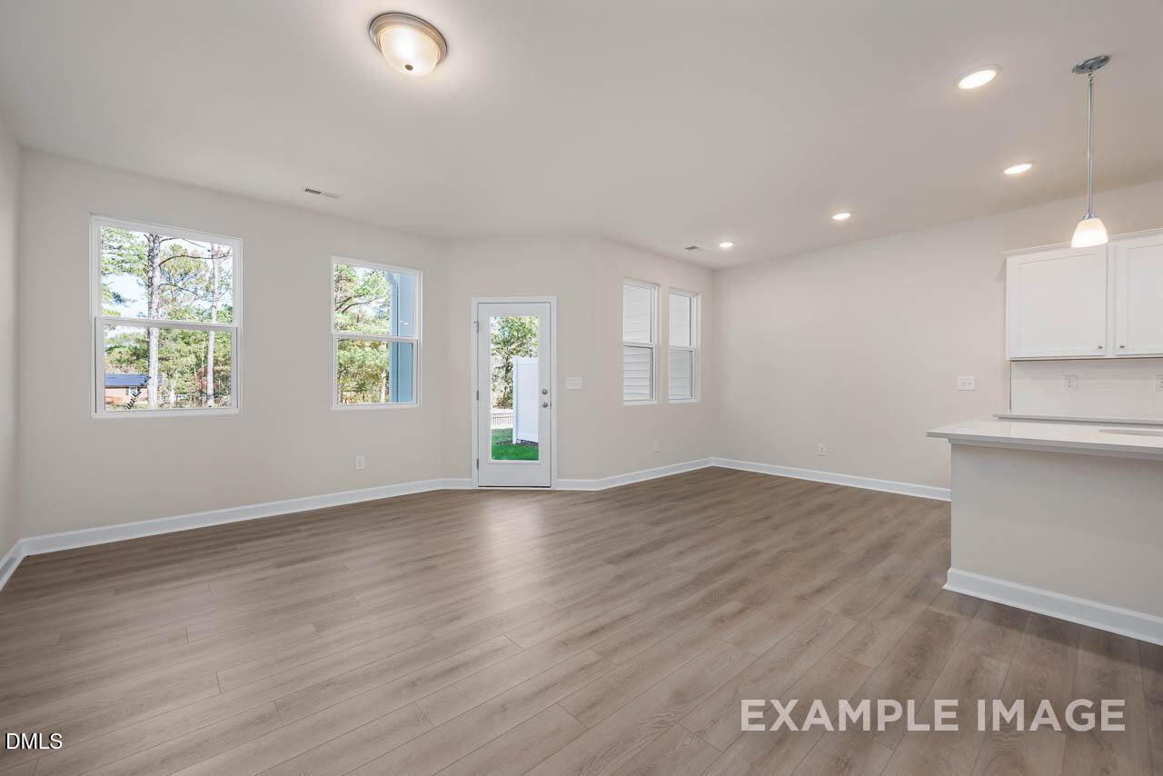 Bright open living area with hardwood floors, large windows, glass door to yard, and white kitchen cabinets in Davidson Homes Graham Interior, Fuquay-Varina