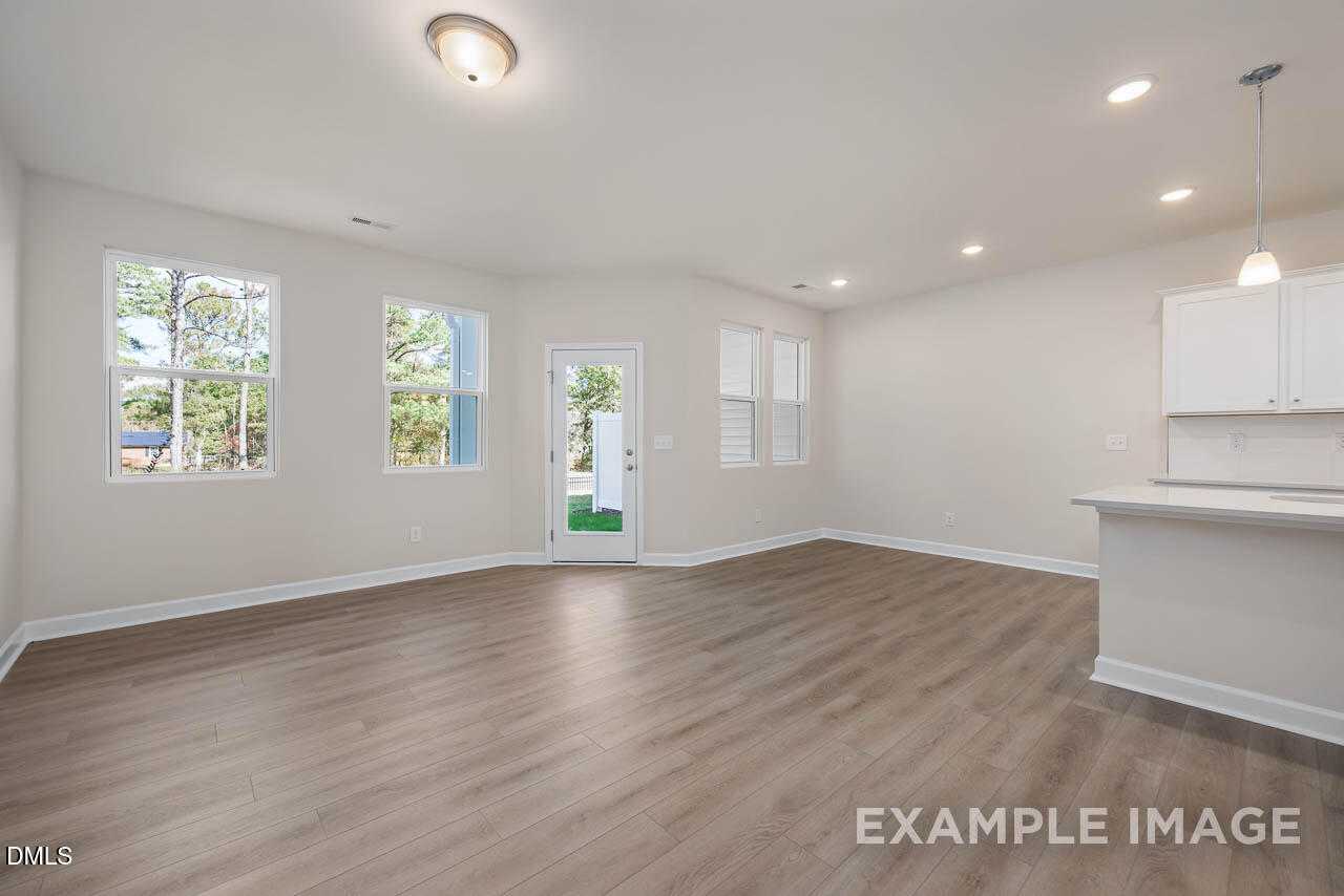 Bright open-concept living and kitchen with light wood floors, white cabinets, large windows, and glass patio door in Davidson Homes The Graham, Fuquay-Varina, NC