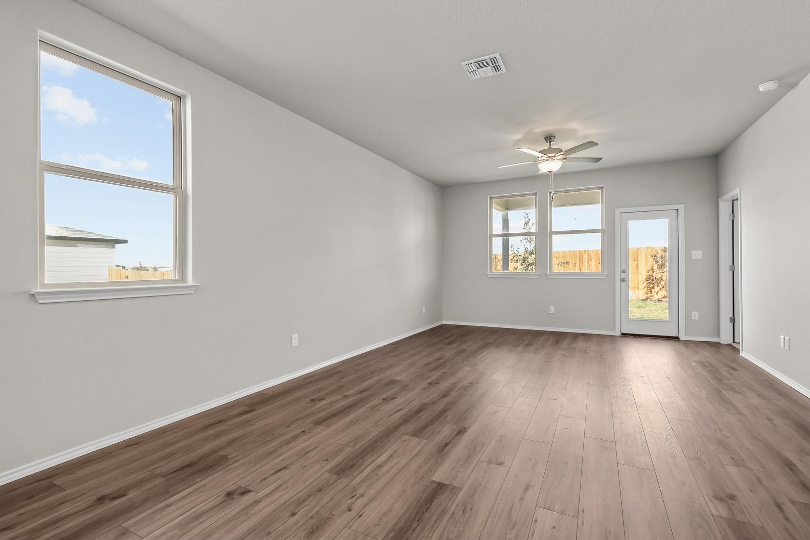 Spacious living area in The Arroyo floor plan featuring wood-look flooring, large windows, and backyard access.