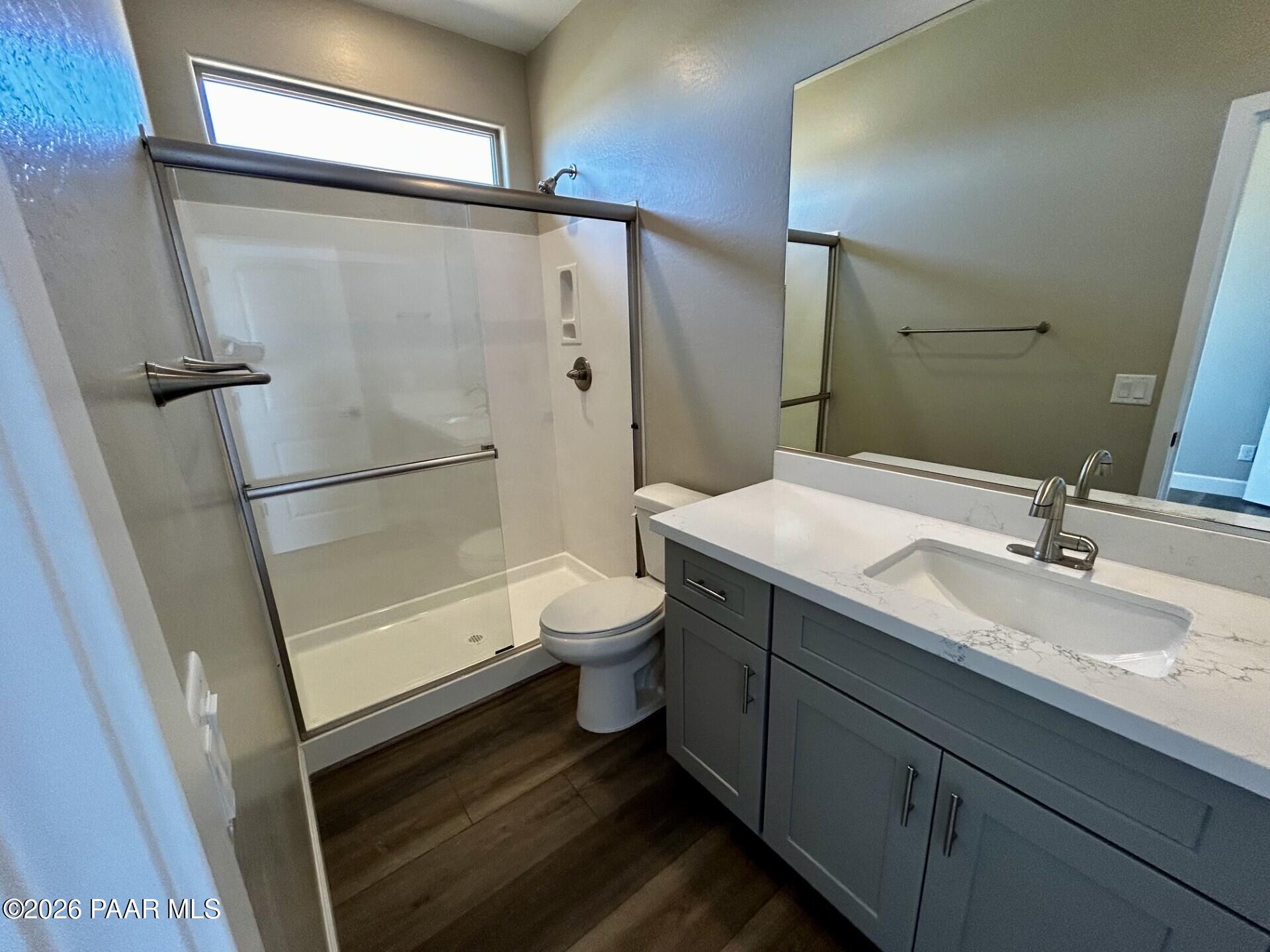 Modern bathroom with frameless glass shower, gray vanity, quartz countertop, and wood flooring in Davidson Homes The Harmony C, Prescott Valley AZ