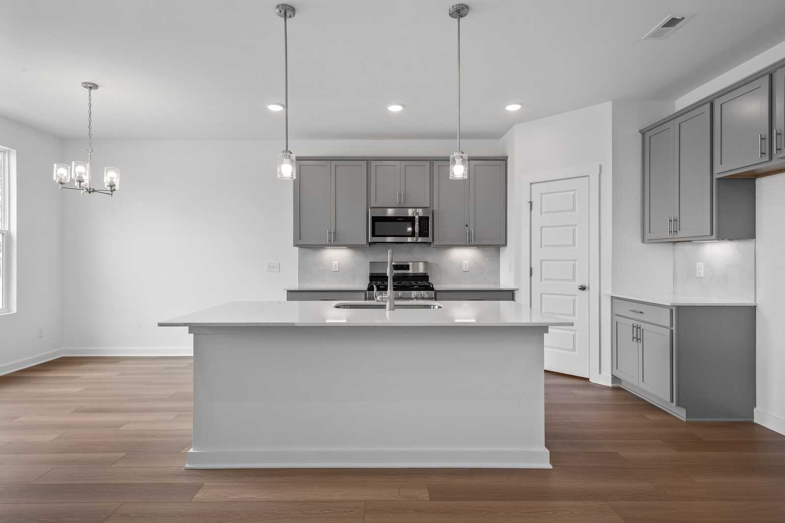Modern kitchen in The Asheville home design with large white island, gray cabinets, and stainless steel appliances