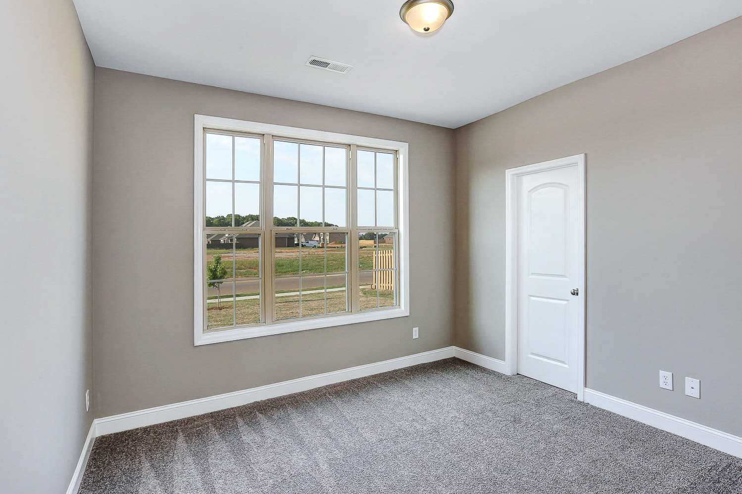Spacious bedroom in The Montgomery home by Davidson Homes, Meridianville AL, with large window overlooking neighborhood, gray walls and carpet
