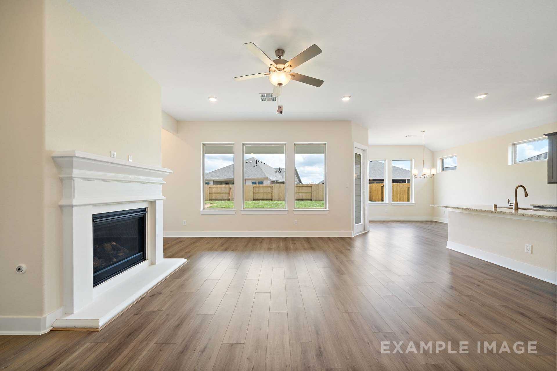 Spacious open-concept living room in The Diana C with white fireplace, large windows, ceiling fan, and adjacent kitchen island