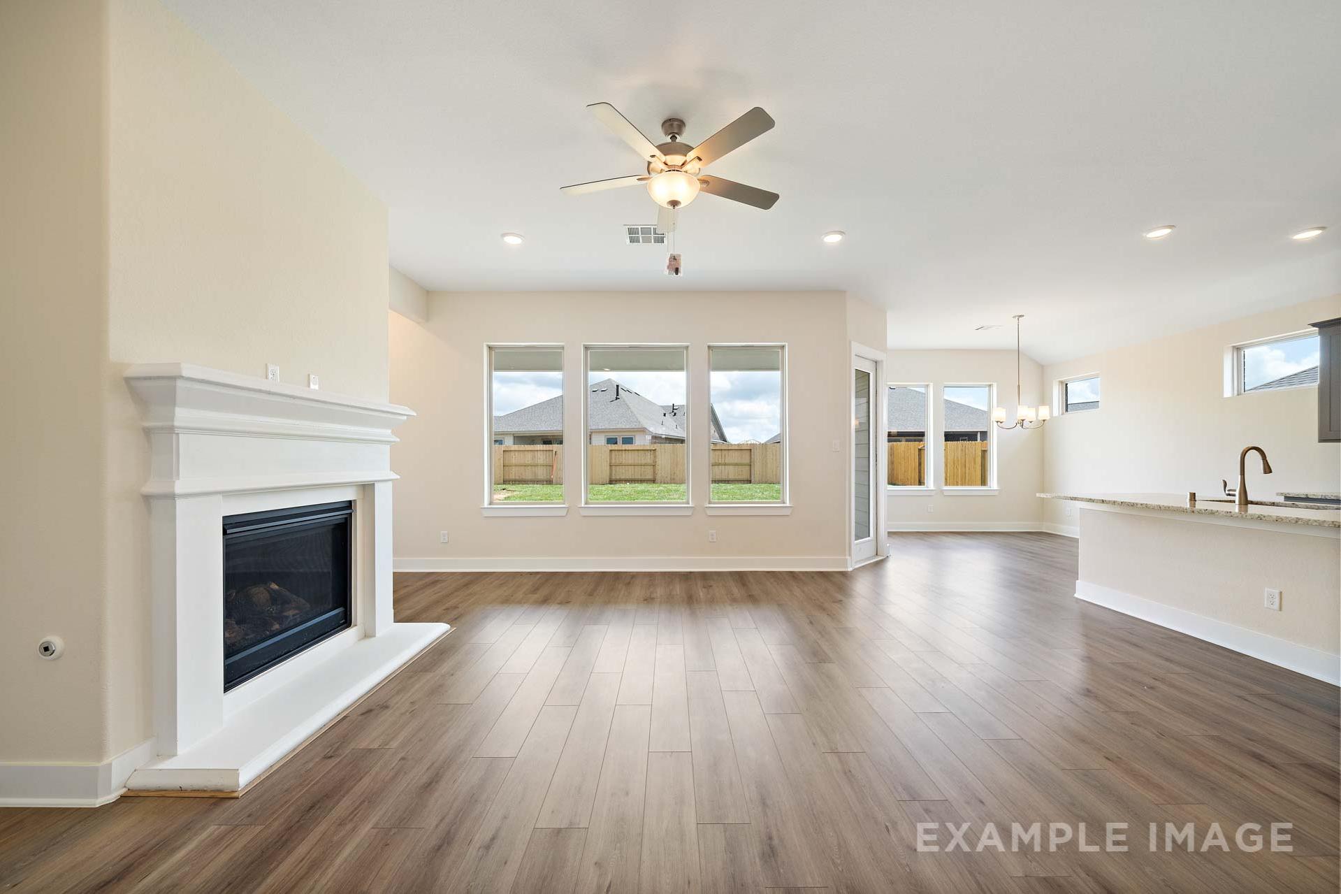 Spacious open-concept living room in The Diana C with white fireplace, large windows, ceiling fan, and adjacent kitchen island