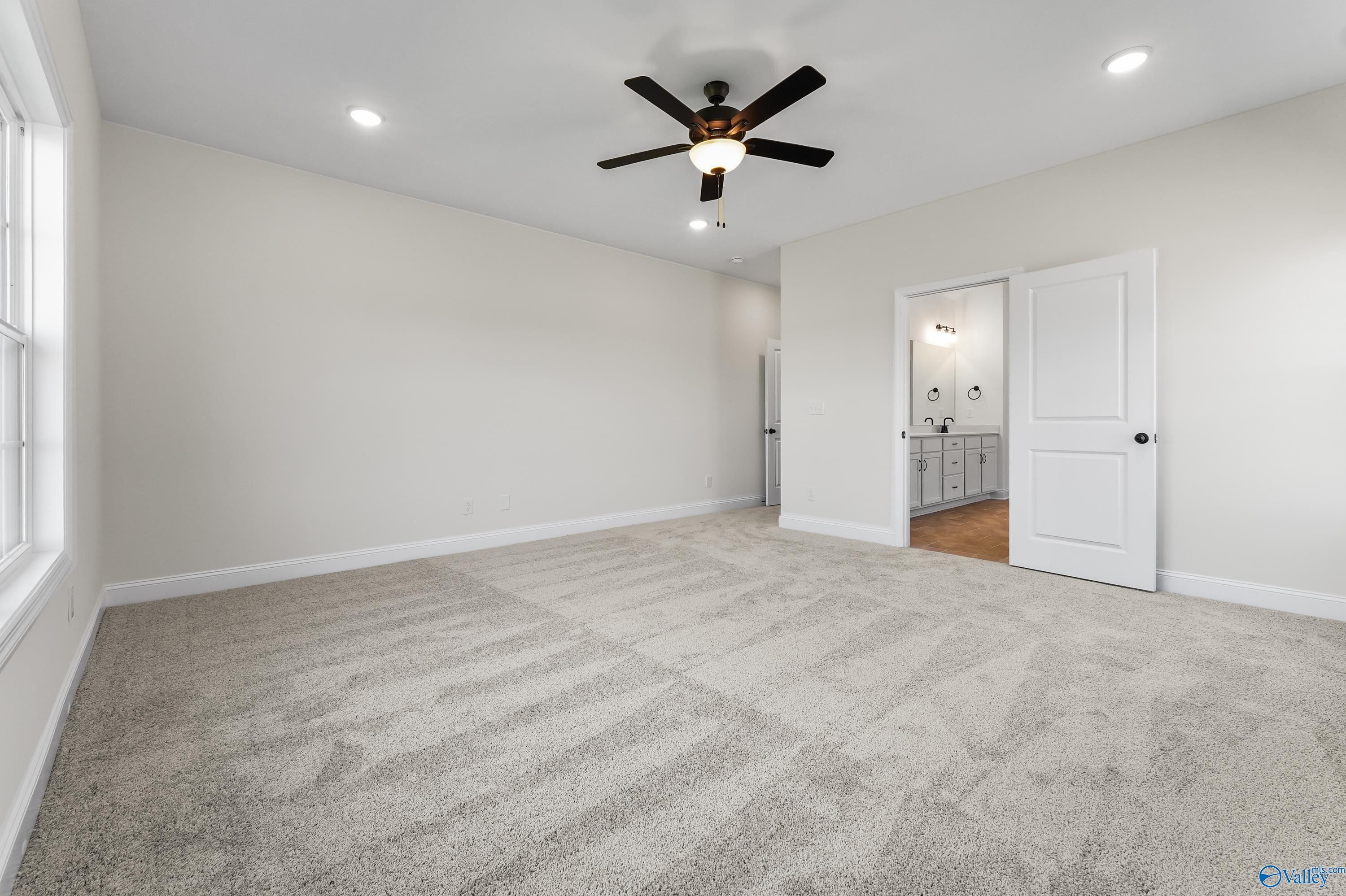 Spacious master bedroom with ceiling fan, beige walls, carpet and en-suite bath in Davidson Homes The Finleigh, Harvest, AL