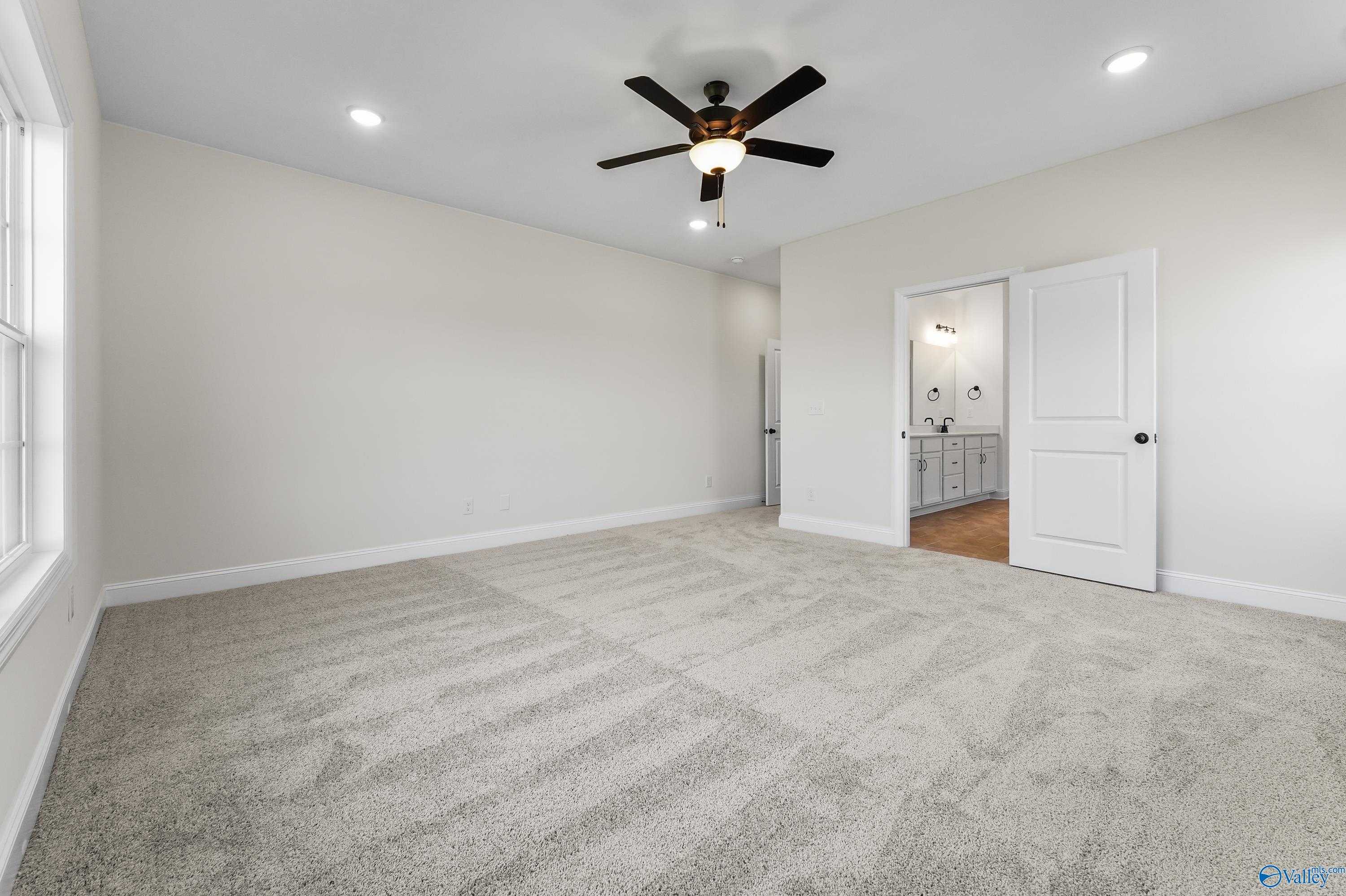 Spacious master bedroom with ceiling fan, beige walls, carpet and en-suite bath in Davidson Homes The Finleigh, Harvest, AL