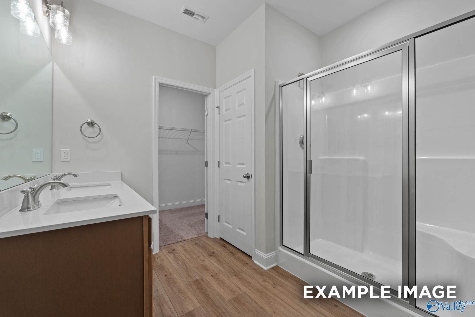 Modern bathroom with double vanity, frameless glass shower, and linen closet in Davidson Homes The Franklin C, Meridianville, Alabama