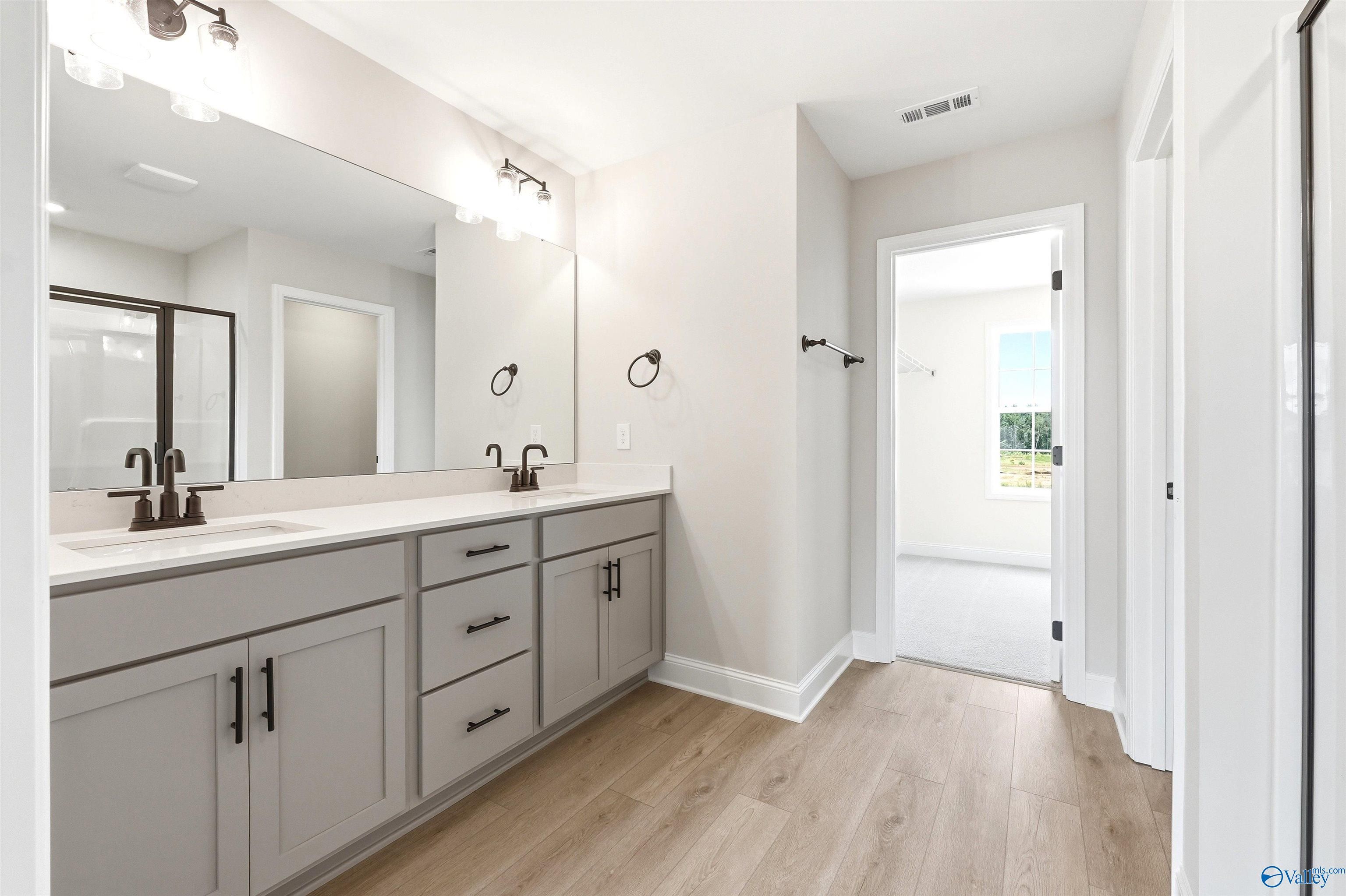 Modern dual-vanity master bathroom with light wood flooring in The Shelby A floor plan at Wood Trail, Toney, Alabama.